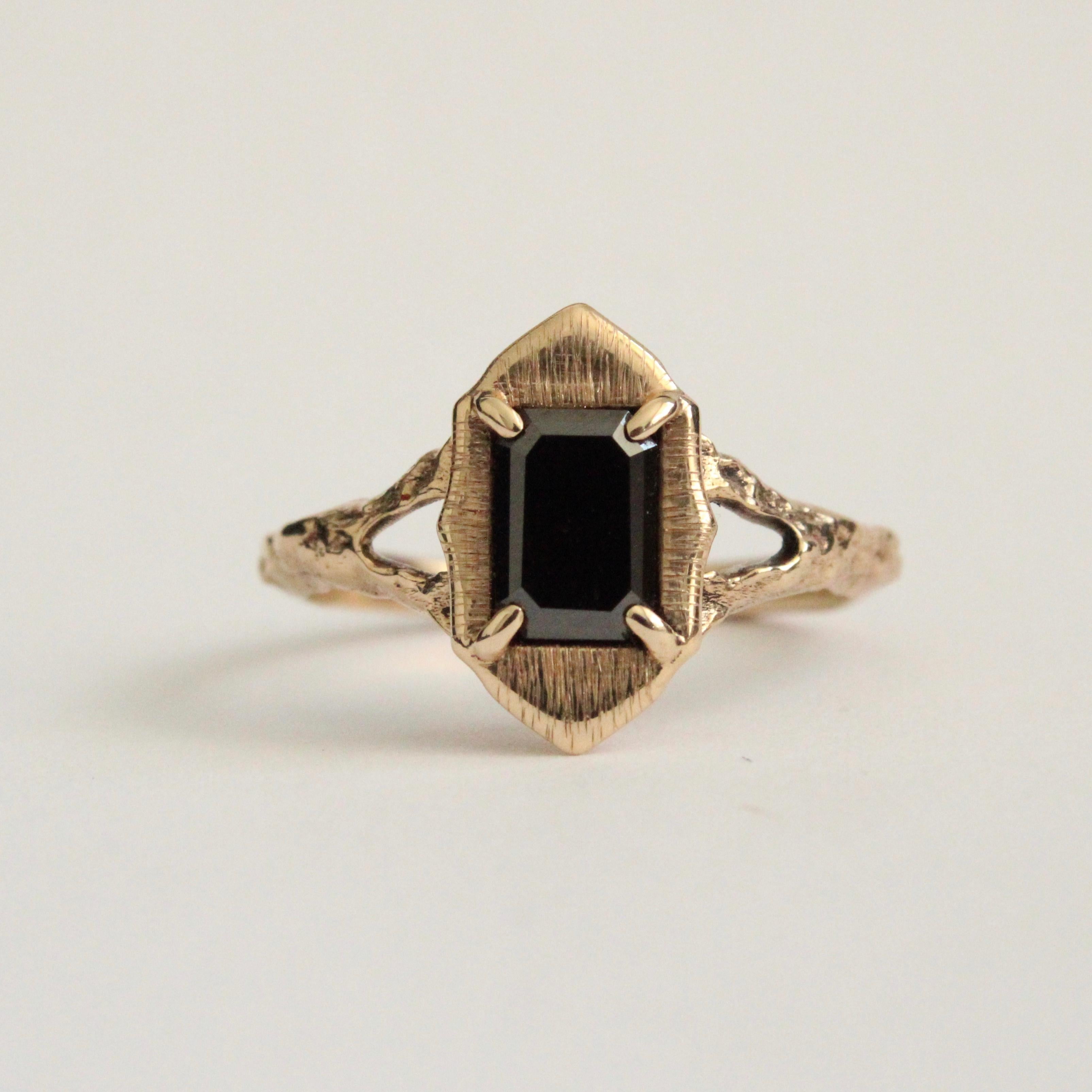 Black diamond ring with a beautiful 7x5mm emerald cut black diamond center stone in 14k yellow gold.  This piece has a beautiful satin halo with a split band. One of a kind size 8. 