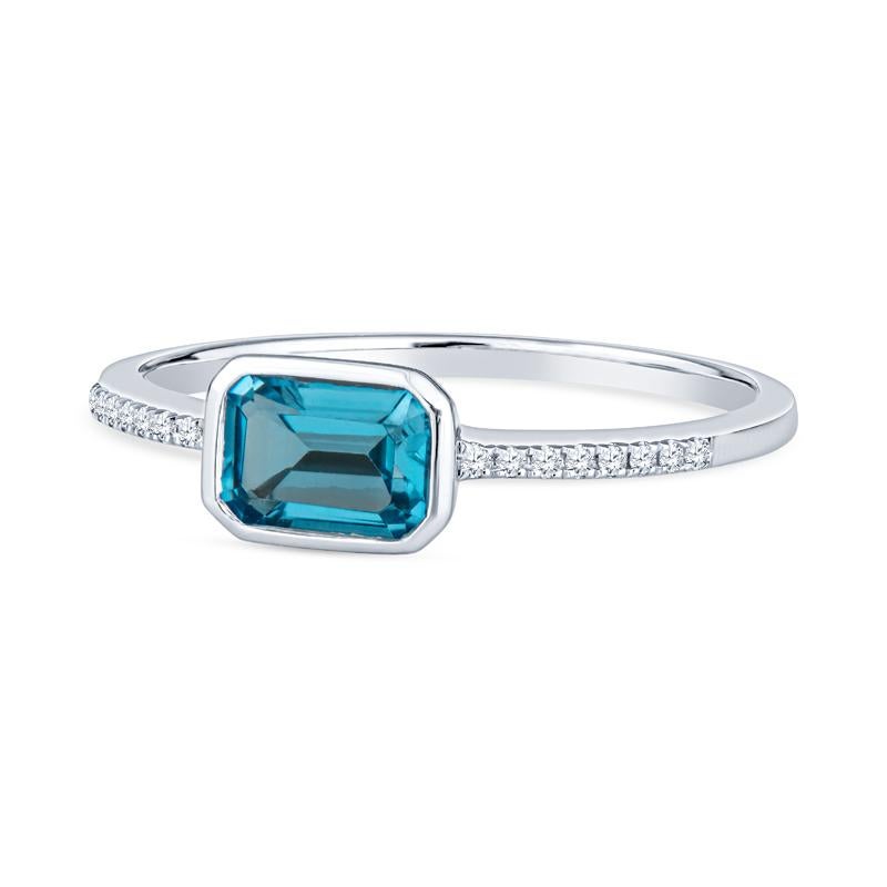 This dainty ring features an emerald cut blue quartz set east-west accented by 0.04 carat total weight in round diamonds on the band set in 14 karat white gold. It is a size 6.5 but can be resized upon request. This ring can be worn alone or stacked