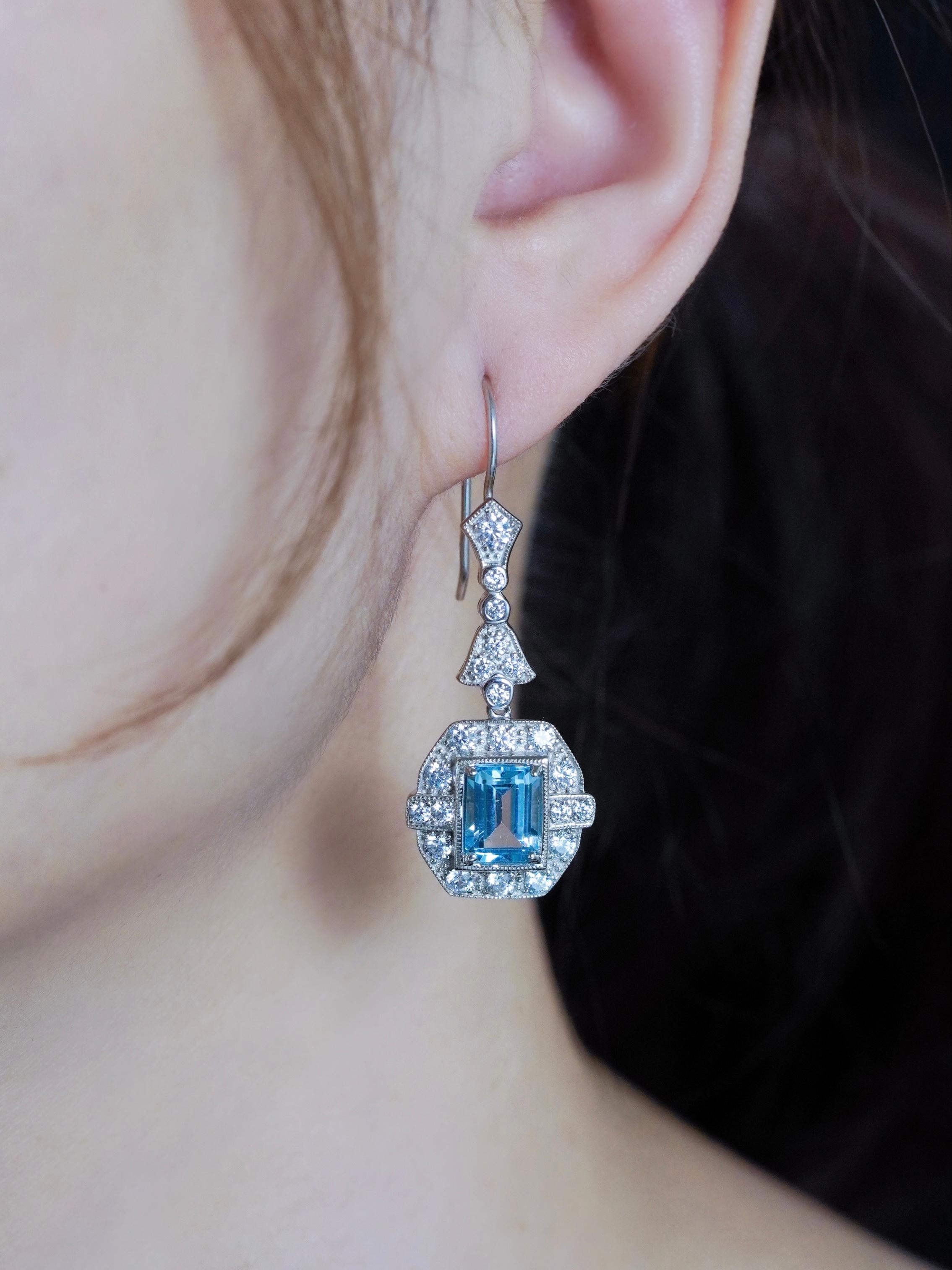 In der Mitte befindet sich ein auffälliger Blautopas im Smaragdschliff, der einen kühlen, lebendigen Glanz ausstrahlt. Jeder Stein ist wunderschön mit funkelnden Diamanten umrahmt, die seine Klarheit und Eleganz unterstreichen. Das Design der
