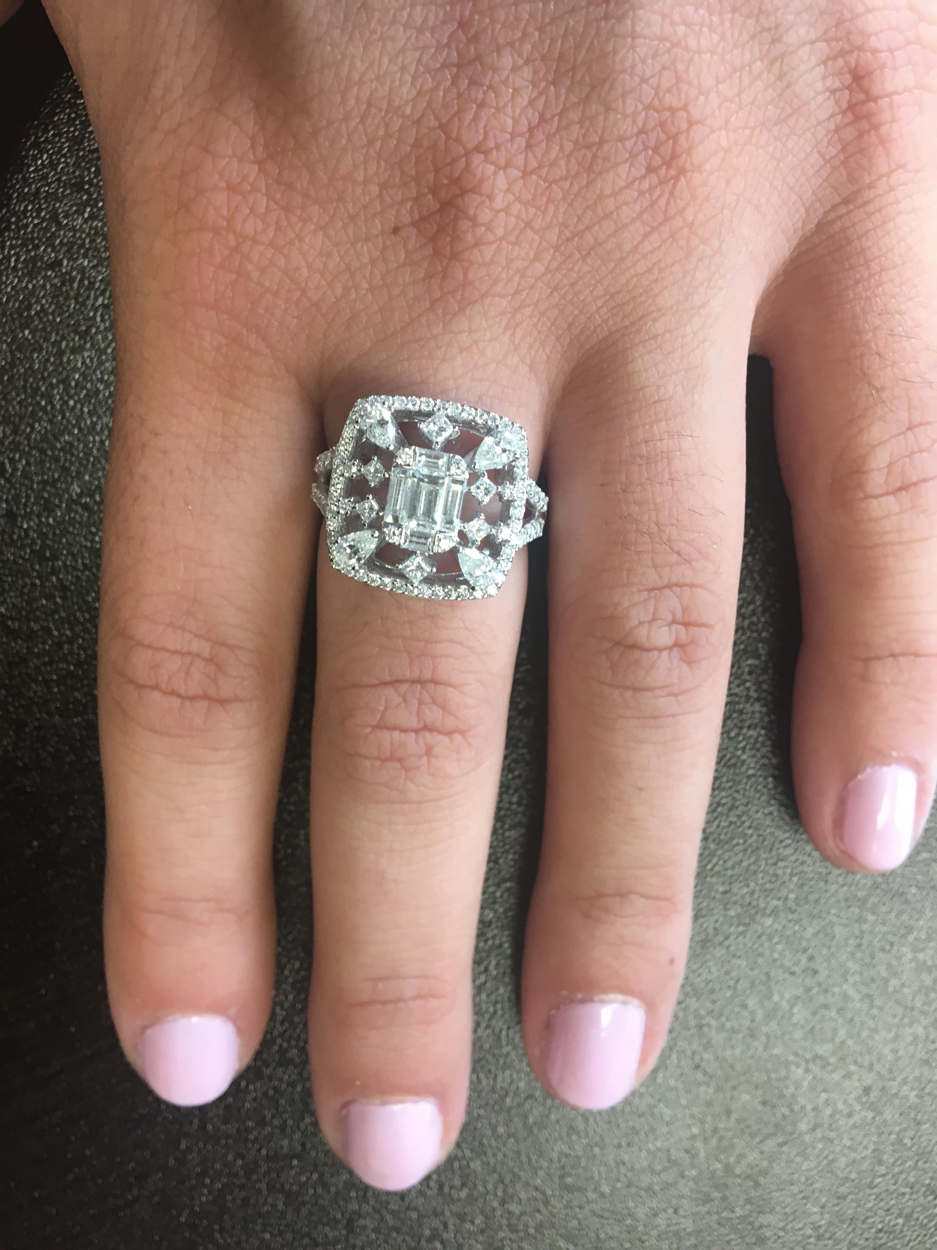 This stunning 18K white gold ring is set with an emerald cut illusion stone in the center, surrounded by multi cut stones. Pair shapes, princesses and round diamonds. It's a unique look and a statement piece. The total carat weight is 1.45 Ct. The