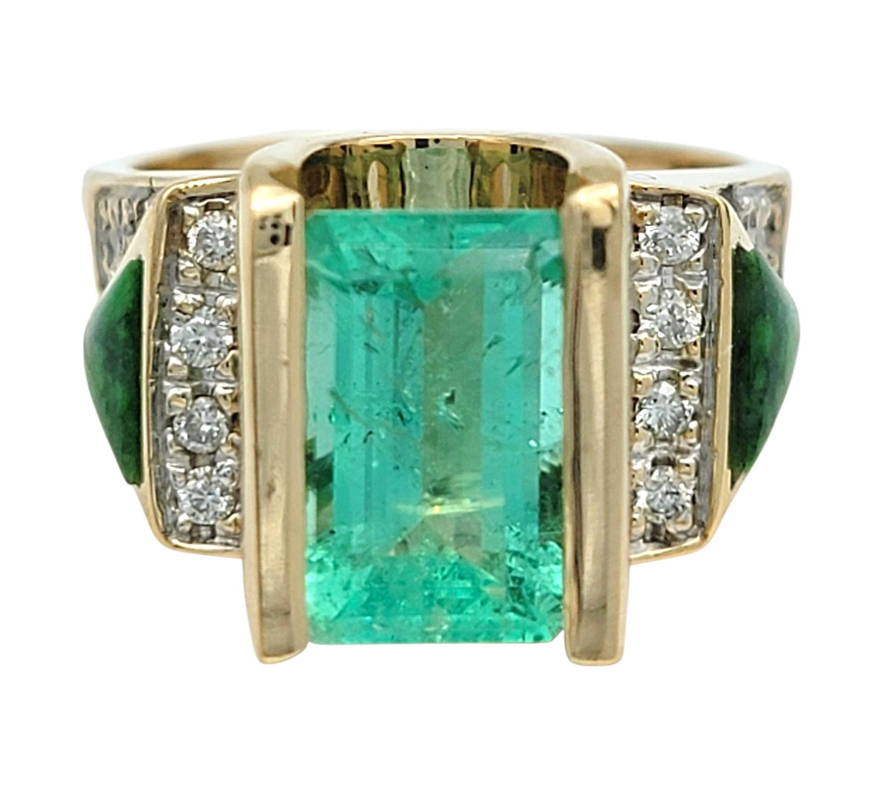 Taille de l'anneau : 7

Cette bague audacieuse et architecturale présente en son centre une émeraude colombienne éclatante, taillée dans une forme classique d'émeraude et sertie dans de l'or jaune 14 carats brillant. Des diamants ronds brillants