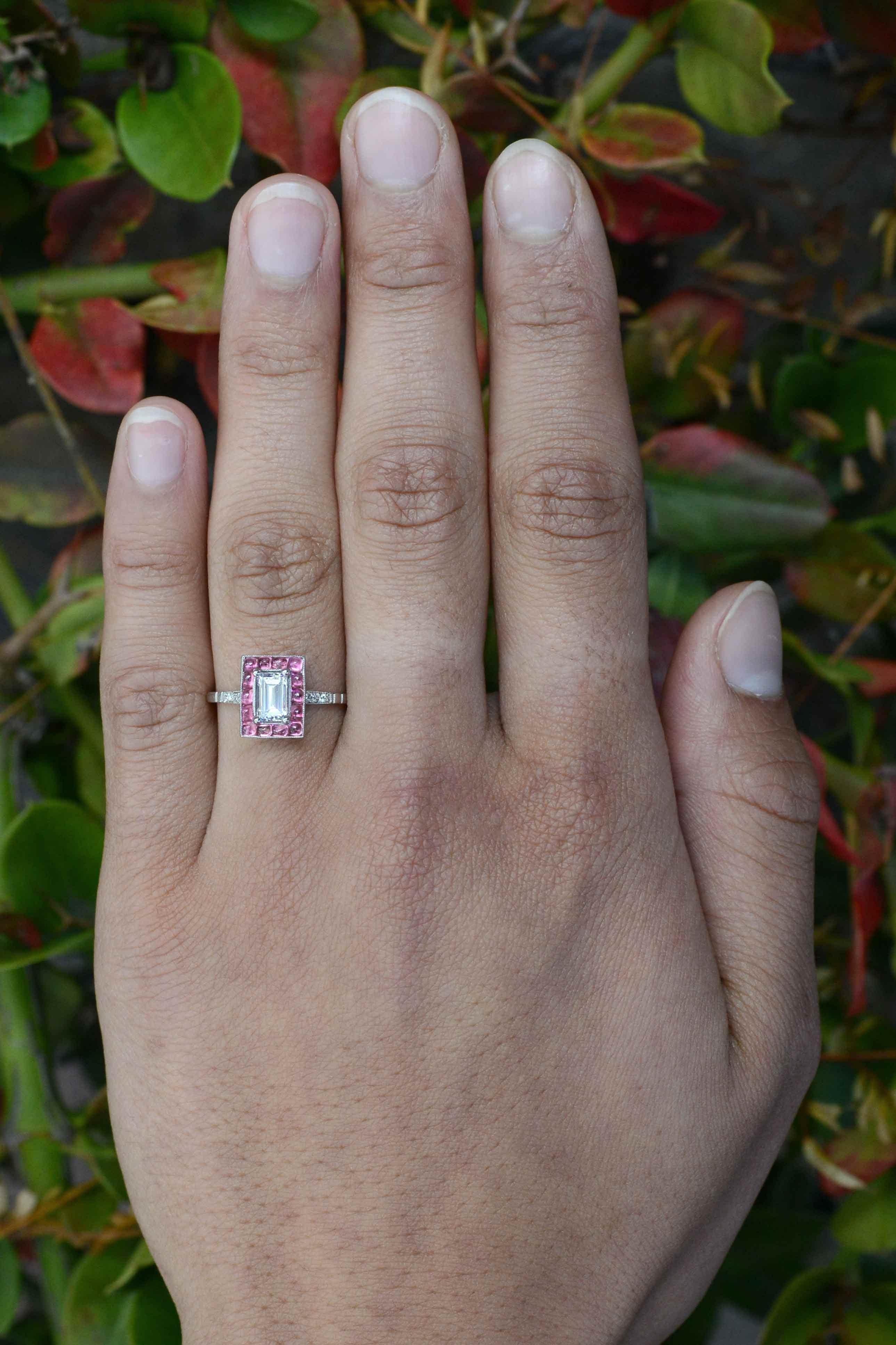 An unforgettable emerald cut diamond Art Deco style engagement ring centered by a dazzling 3/4 carat step cut with exceptional clarity and brilliance. Smartly surrounded by a halo of 14 of the cutest pink sapphire cabochons that lend an elegant