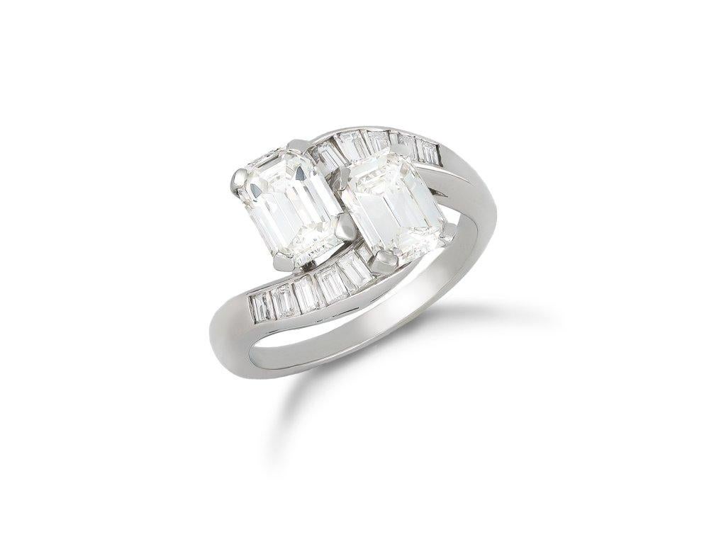 Emerald-cut diamond cross over ring. Set with two octagonal emerald-cut diamonds in open back claw settings, with a combined approximate diamond weight of 2.25 carats, flanked by ten rectangular baguette cut diamonds in open back channel settings
