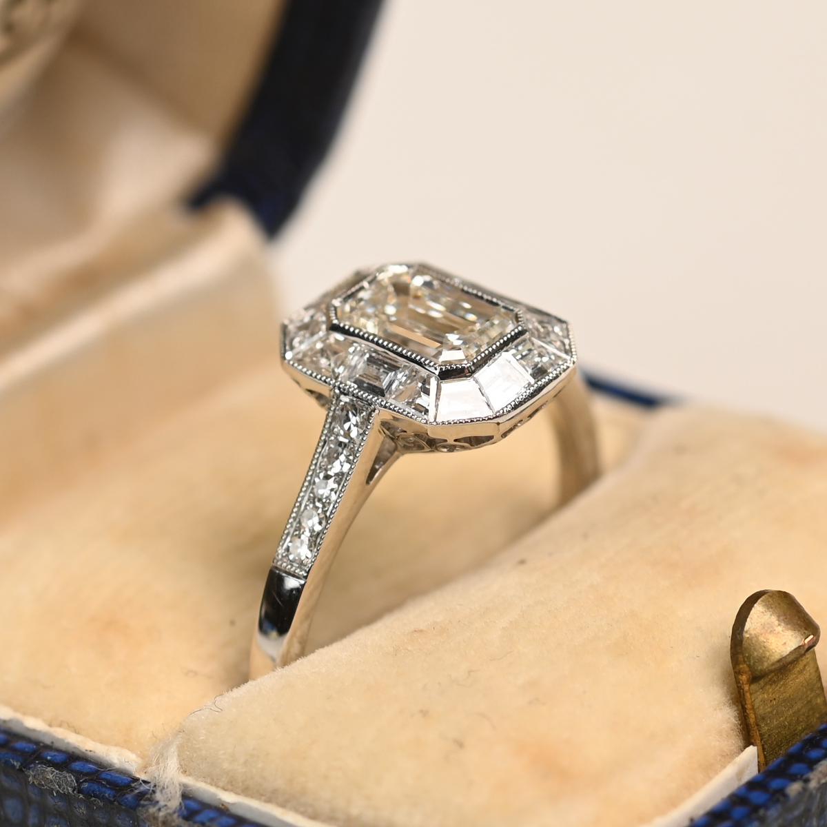 In der Mitte dieses Platinrings befindet sich ein Diamant im Smaragdschliff, der sicher in die Lünette gefasst und von GIA mit einem Gewicht von ca. 0,8 Karat, Farbe H und Reinheit VS2 zertifiziert ist. Der Mittelstein ist von einem Halo aus