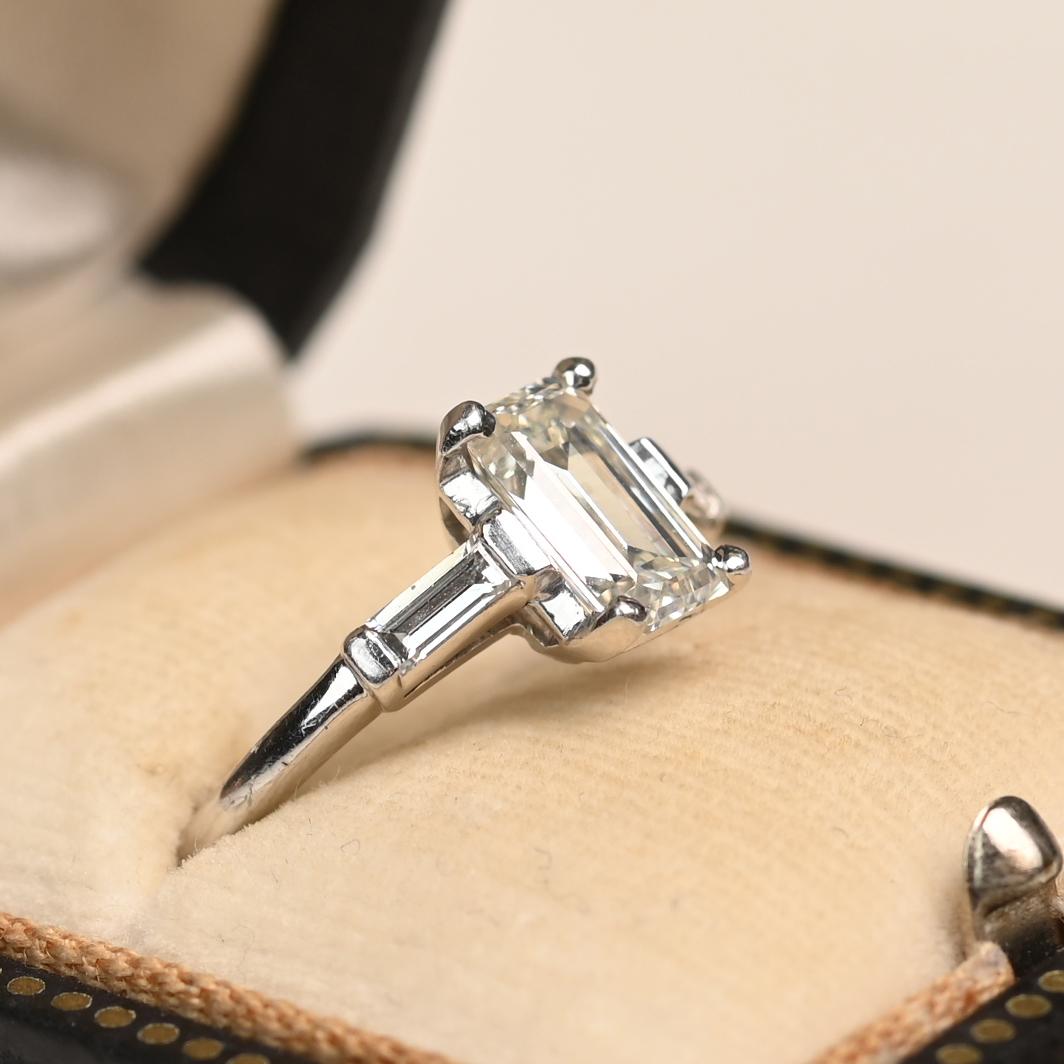 This elegant ring showcases an approximately 1.20-carat emerald-cut diamond of J color and SI1 clarity, gracefully set in a classic four-prong setting. The clean lines of the emerald cut emphasize the diamond’s clarity and brilliance, offering a