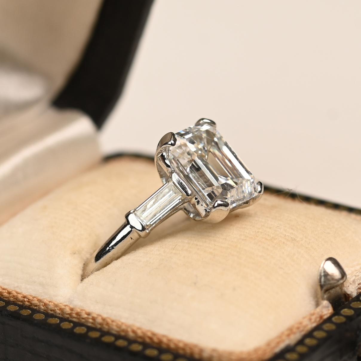 This exquisite vintage ring showcases a GIA-certified emerald-cut diamond weighing approximately 3.00 carats, boasting an exceptional H color and VS1 clarity. The diamond is securely held in a classic prong setting, allowing maximum light to reflect