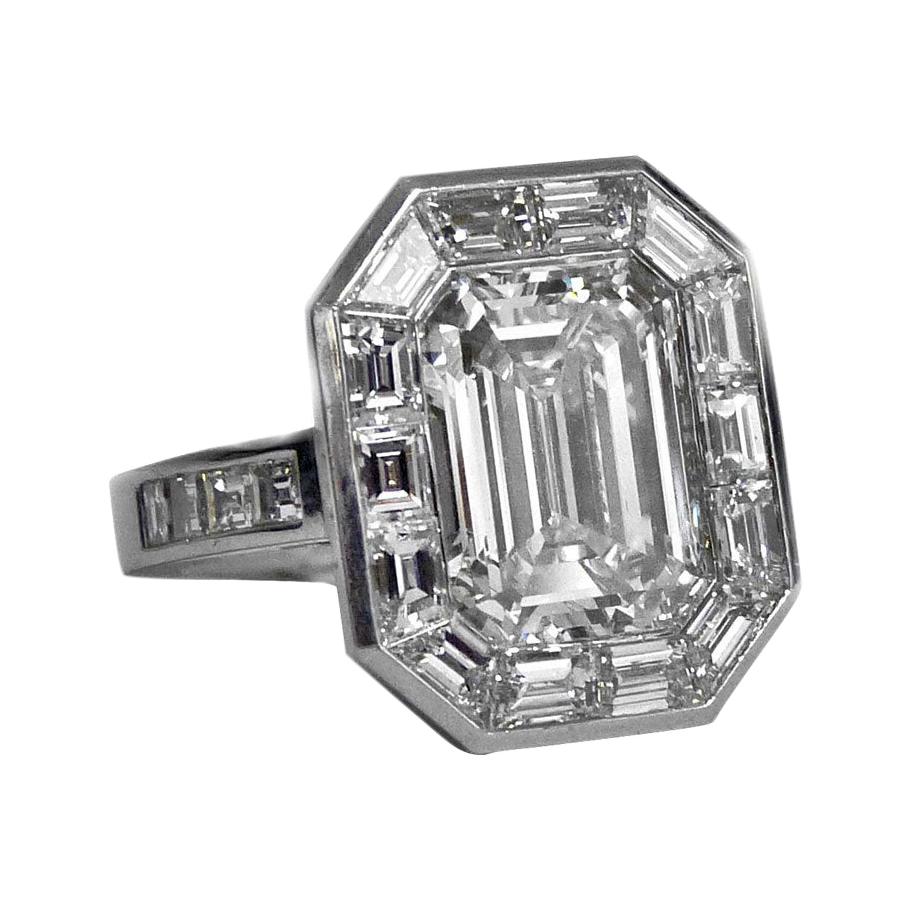 An Unusual Emerald Cut Diamond Platinum Ring.
The Center Emerald Cut Diamond weighing 4.14 Carats, I Color, VS1 sits within a border of emerald cut diamonds supported by emerald cut diamonds to the shoulders . The mount is platinum and bears no