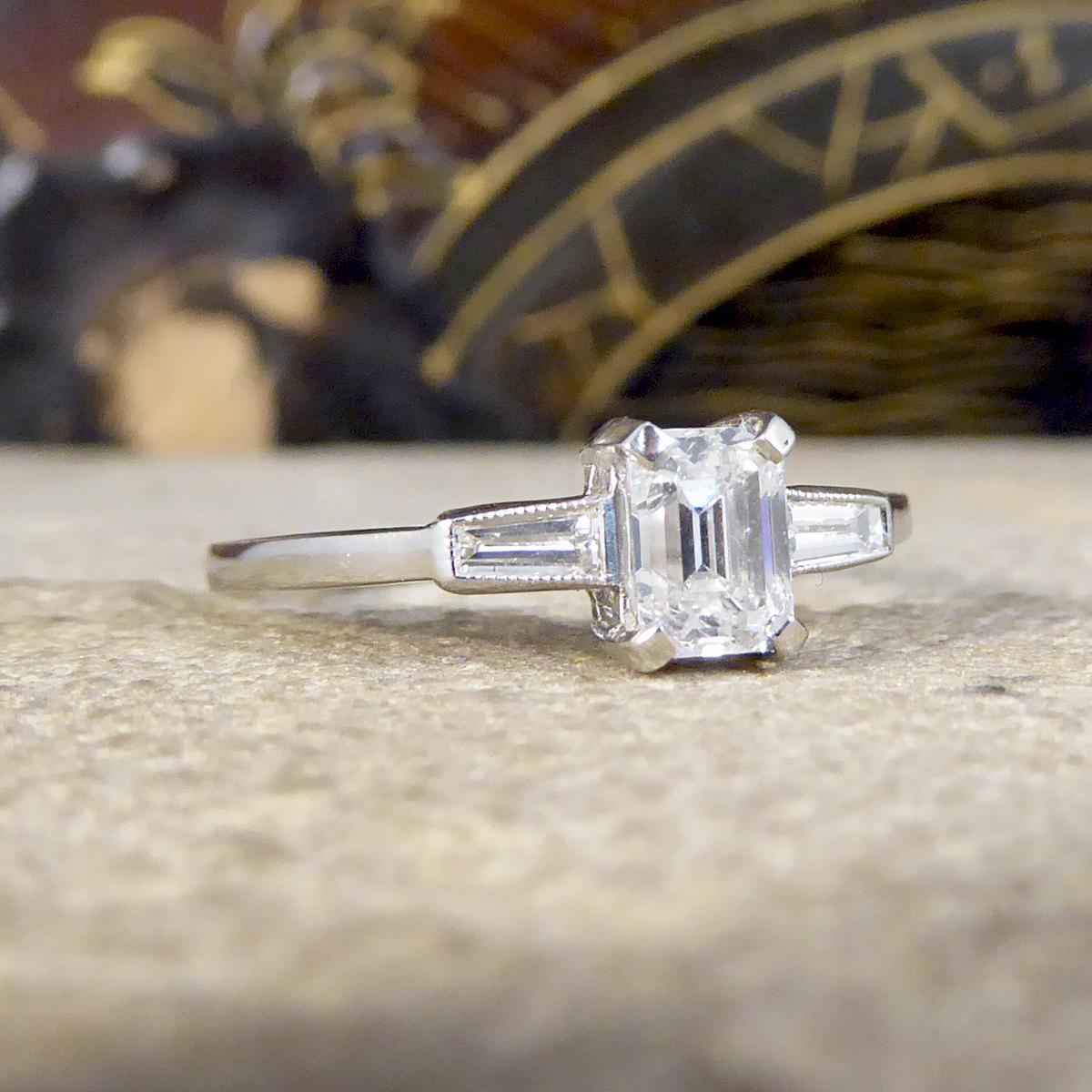The perfect contemporary engagement ring has such a lustrous sparkle holding a very bright and clear Emerald Cut Diamond centre. It weighs 0.52ct in the centre with Tapered Baguette Cut Shoulders either side. Showing great colour and clarity it