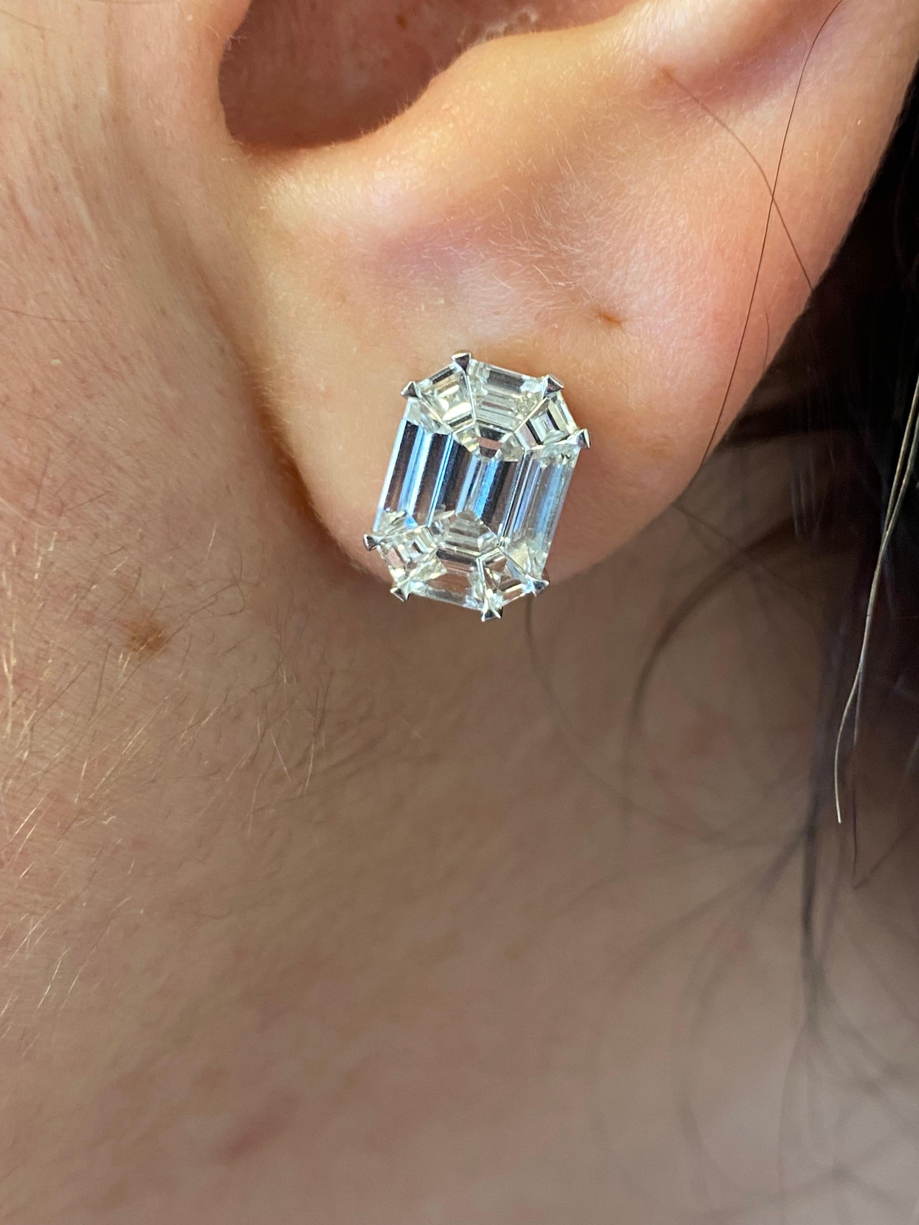Emerald cut cluster earrings set in 18K white gold. The earrings are set in an illusion that creates the look of a 7 carats total emerald cut studs look. The earrings are set with emerald, baguette and trapezoid diamonds. The color of the stones are