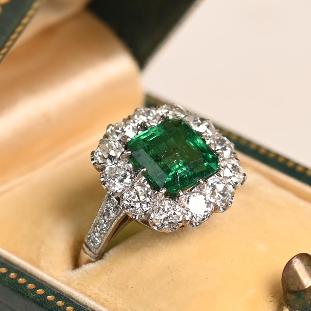 Este exquisito anillo exhibe una impresionante esmeralda natural de aprox. 2,40 quilates, tallada expertamente en forma de esmeralda y asegurada por delicadas garras. La rica tonalidad verde de la piedra central se complementa maravillosamente con