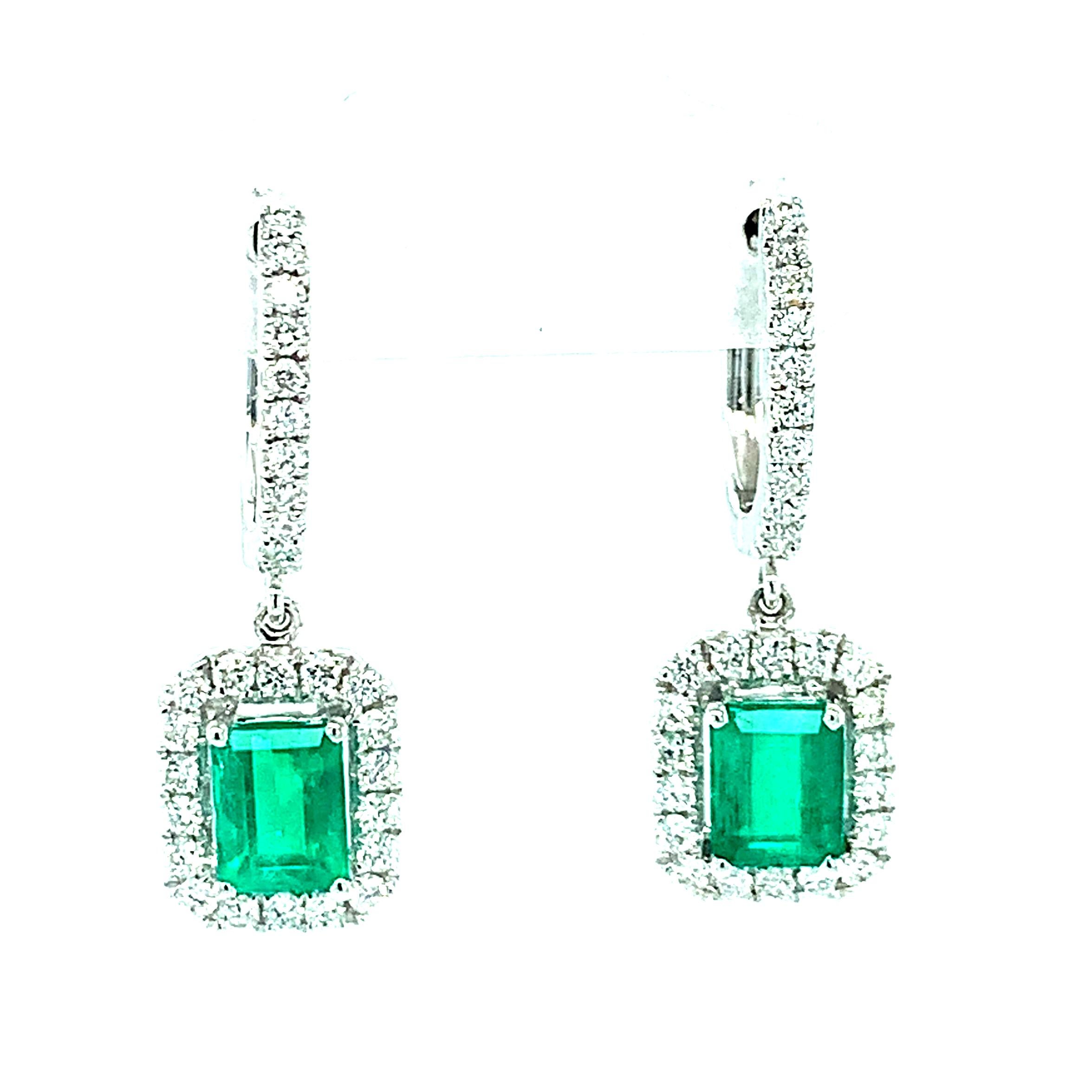 These gorgeous emerald and diamond earrings are a luxurious statement of classic elegance and style! Two brilliant, rich green emerald-cut emeralds are set in bright 18k white gold, surrounded by a sparkling halo of round brilliant white diamonds.