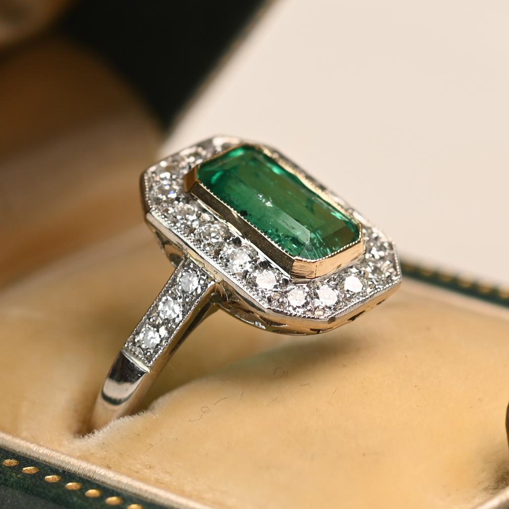 This exquisite elongated platinum ring features a vibrant emerald-cut emerald weighing approximately 1.40 carats. The striking green center stone is secured in an 18k yellow gold bezel, creating a bold and elegant contrast. Surrounding the emerald