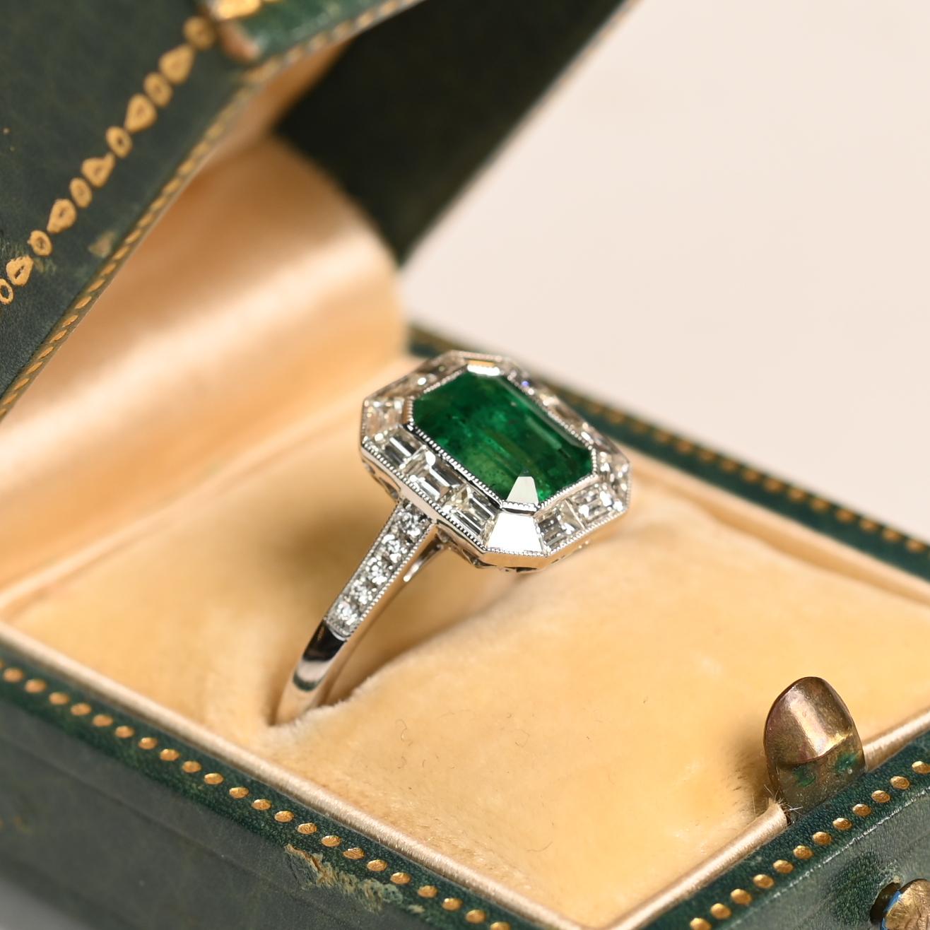 Questo squisito anello mette in mostra uno splendido smeraldo dello Zambia da circa 1,50 carati, incastonato nel platino. La vibrante pietra centrale verde è elegantemente incorniciata da un'aureola di diamanti taglio baguette, per un totale di