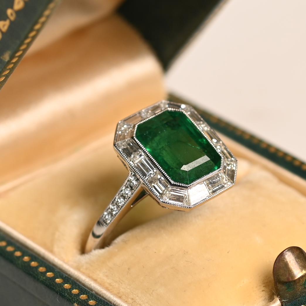 Este exquisito anillo exhibe como pieza central una esmeralda talla esmeralda de aprox. 2,60 quilates certificada por el GIA, engastada en un elegante y seguro engaste de bisel. La esmeralda exhibe un matiz rico y vibrante con una profundidad