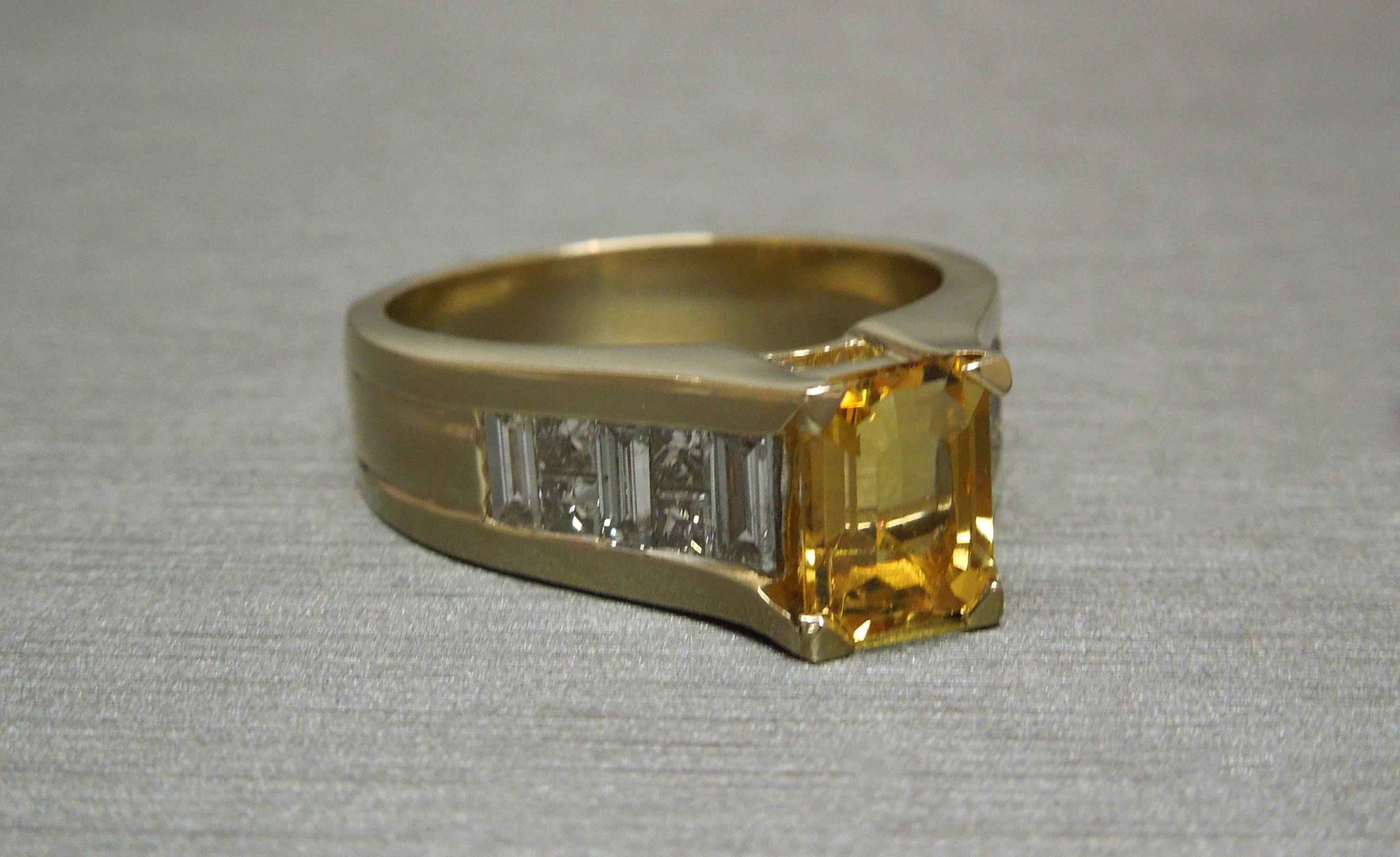Constructed completely of 14KT Yellow Gold in an Art Deco inspired pyramid design featuring a central 1.38 carat Emerald cut coveted Natural Golden Beryl at 7mm x 5.4mm securely set in four prongs. Side sections flanked with a total of 6 Channeled