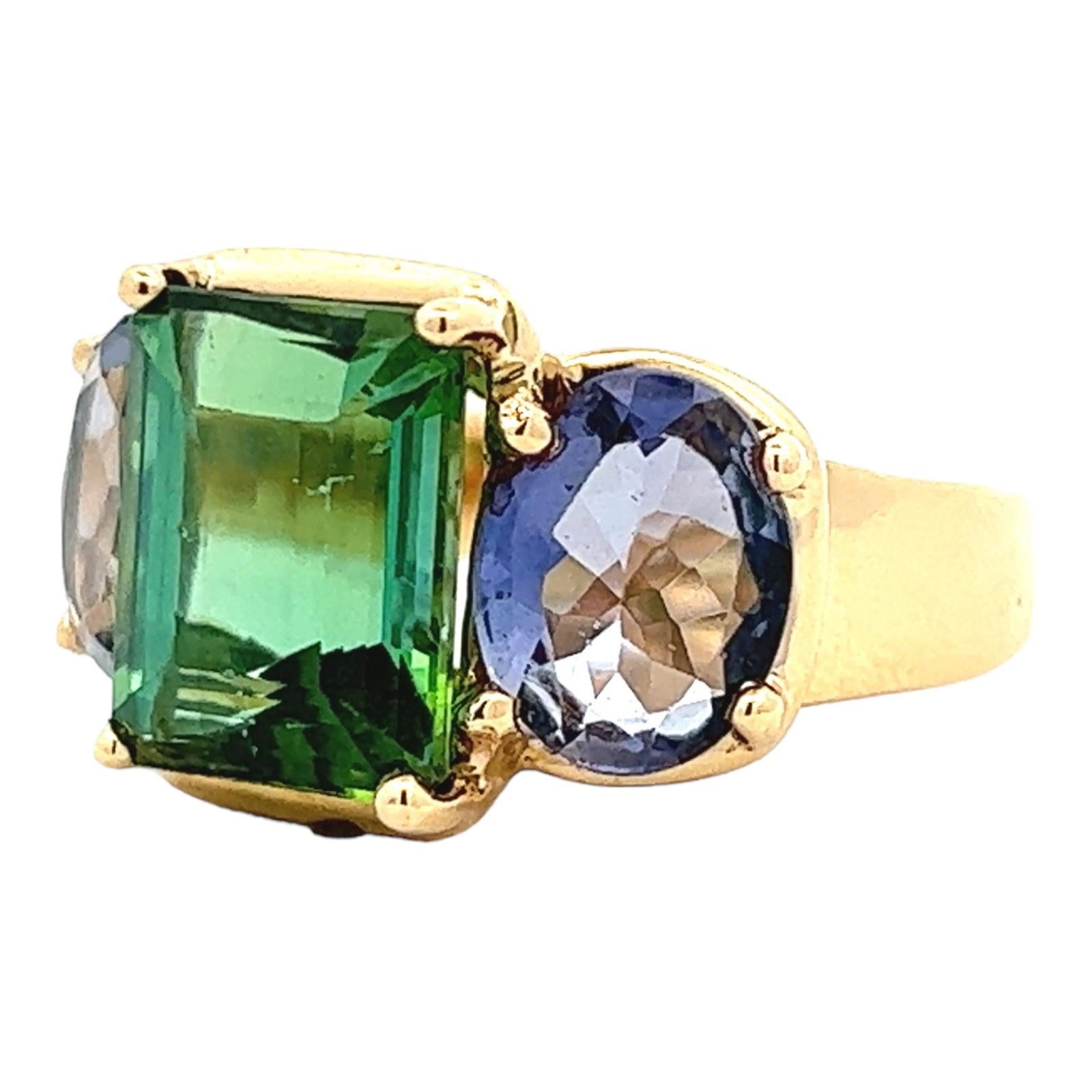 Beautiful green tourmaline and tanzanite cocktail ring handcrafted in 18 karat yellow gold. The colorful gemstone ring features an approximately 6 carat emerald cut green tourmaline gemstone flanked by two oval tanzanite gemstones weighing