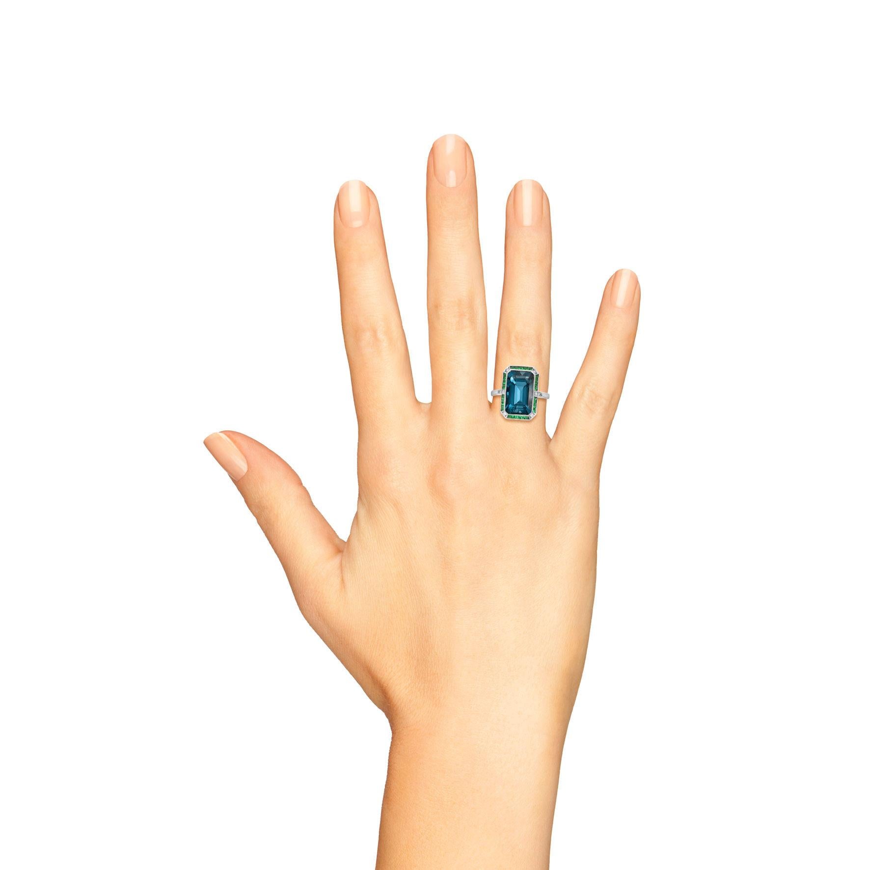 An Art Deco inspired 18K White Gold London blue topaz with emerald and diamond ring. The ring consists of one central emerald cut London blue topaz surrounded by French cut emeralds and round cut diamonds. 

Ring Information
Style: Art-deco
Metal: