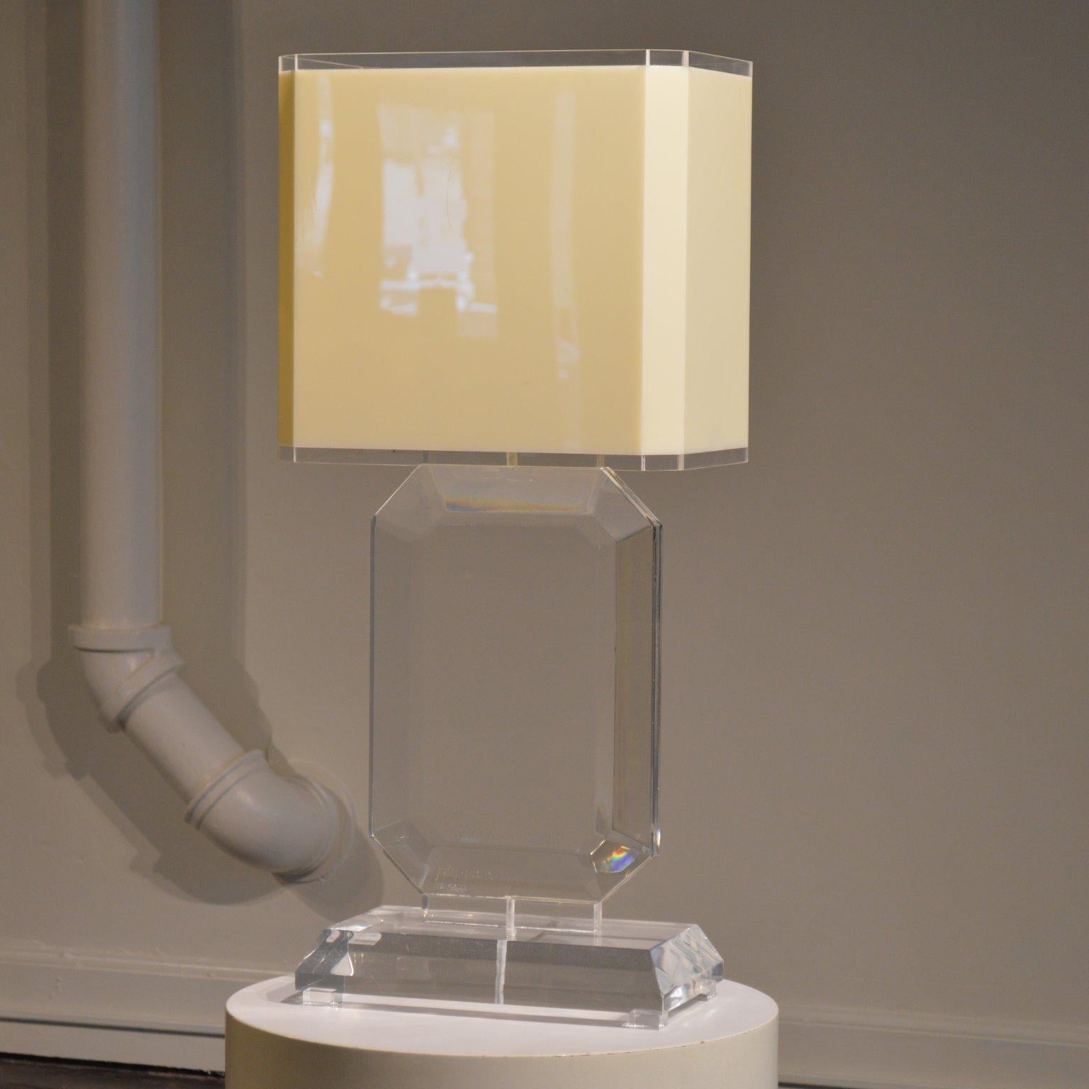 Glamorous Lucite table lamp cut in a large Emerald gem shape. This 1970's lamp features its original cream-colored rectangular acrylic shade. The substantial scale of the piece makes it the highlight of any room. It would work nicely in a bedroom or