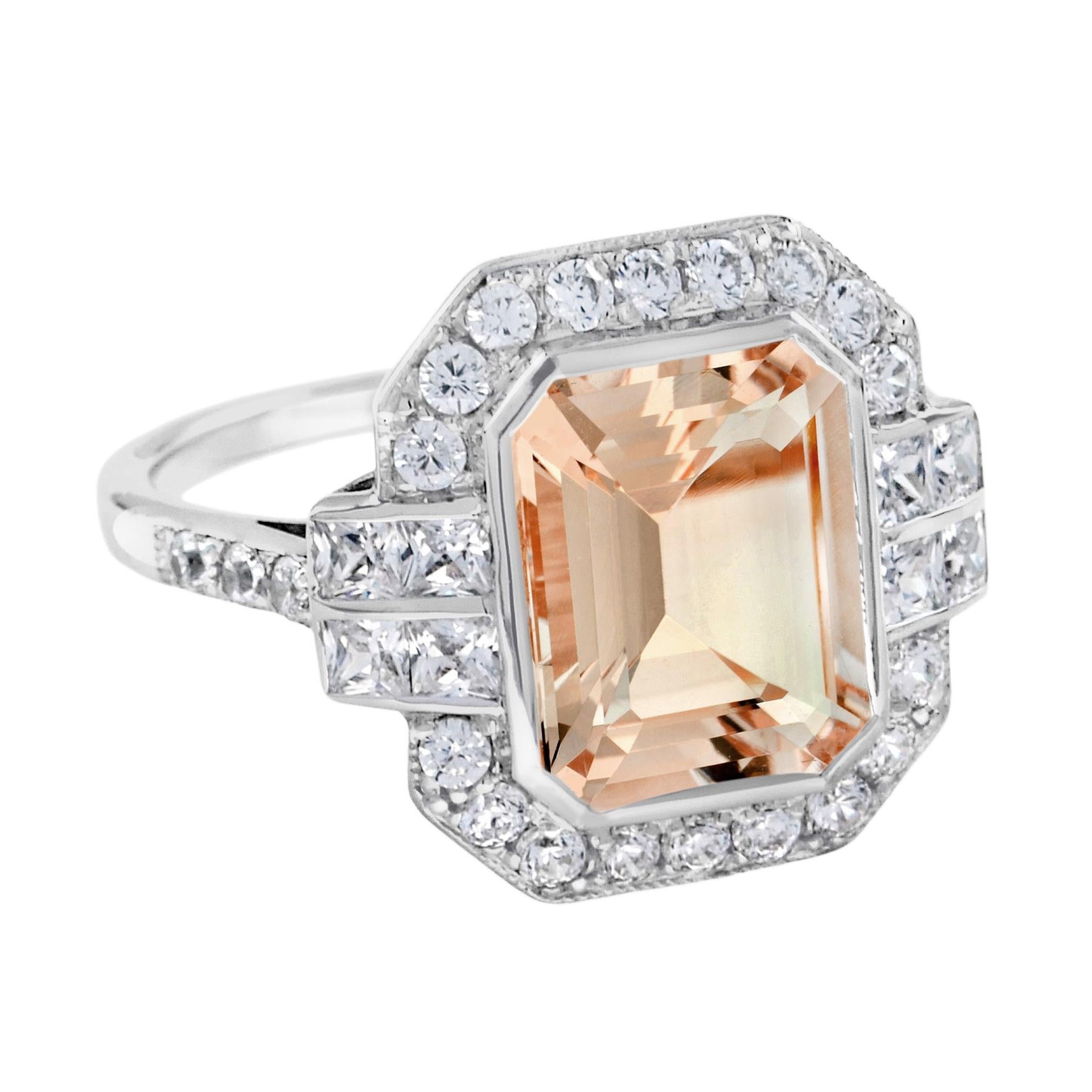 A gorgeous emerald cut morganite is presented in classic Art Deco style. The glorious gemstone radiates from within a sparkling halo of bright round brilliant cut diamonds punctuated east and west with two lines of square diamonds, leading to a