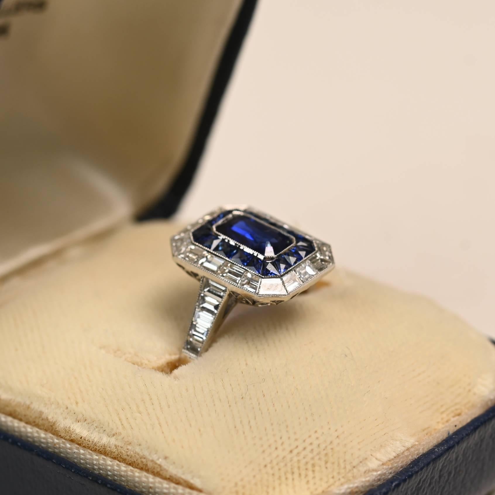 Questo squisito anello in platino mette in mostra un vibrante zaffiro taglio smeraldo senza calore del peso di circa 0,80 carati. La pietra centrale è circondata da un'impressionante doppia aureola - una fila interna di zaffiri taglio francese e una