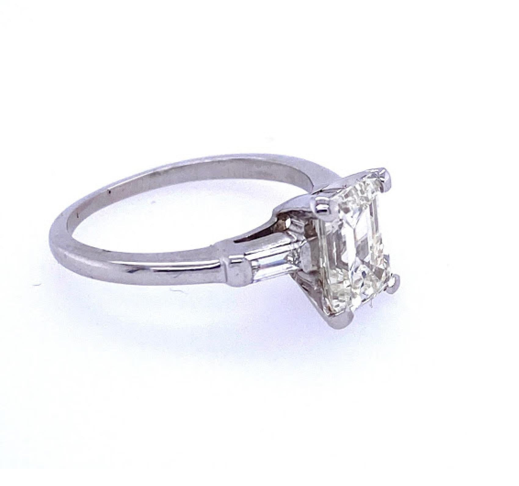  Platinum and diamond engagement ring the center stone is an emerald cut diamond weighing approximately 1.91 carats measuring 8.5x6.3mm being of color grade L and Clarity grade SI1, set in a classic basket head setting flanked by two baguette