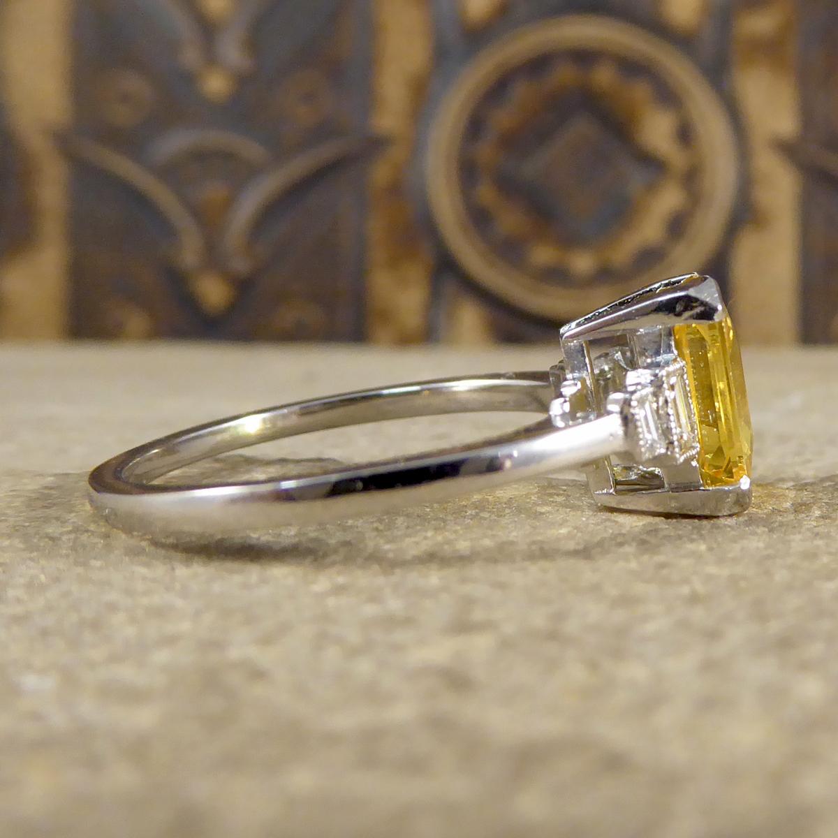 This ring is featuring a beautiful vibrant Emerald cut Yellow Sapphire gemstone weighing 2.10ct in a four claw setting. Accompanied by two Baguette cut Diamonds graduating in size on each side of the Yellow Sapphire in a Millegrain rub over collar