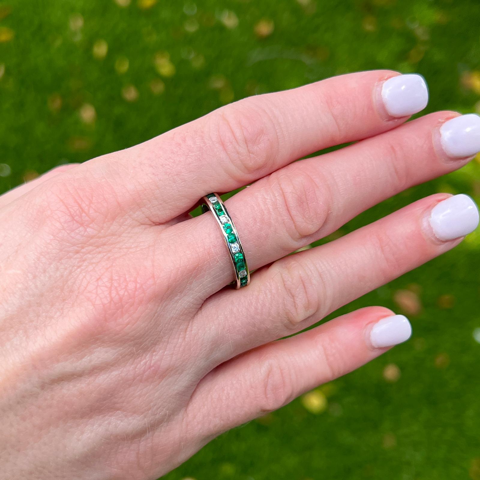 Emerald and diamond eternity band crafted in 18 karat white gold. The band features 10 round brilliant cut diamonds and 20 round cut emeralds. The diamonds weigh approximately .40 CTW and the emeralds approximately .80 CTW. The ring measures 3.5mm