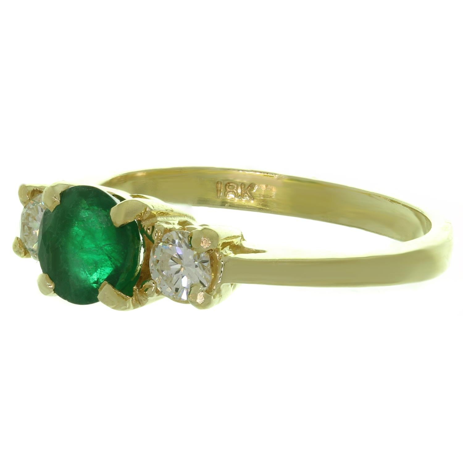 This classic estate 3-stone ring is crafted in 18k yellow gold and set with with a genuine round 6.0mm green emerald in saturated deep green color with open imperfections, weighing an estimated 0.80 carats, and 2 brilliant-cut round Si clarity G-H