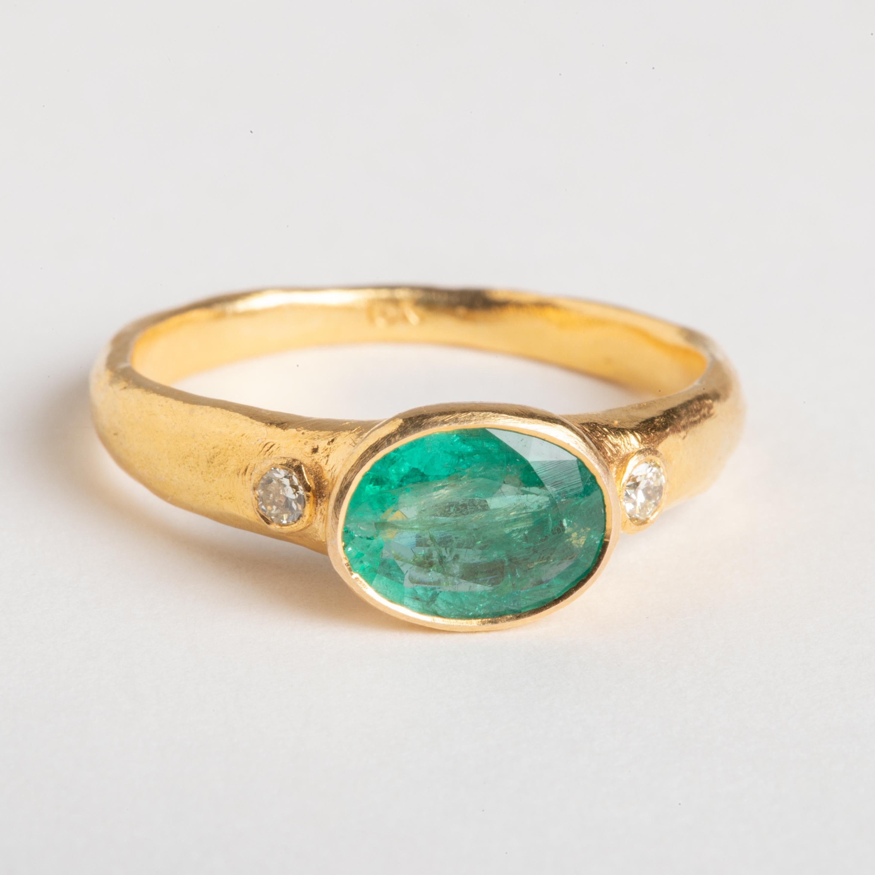 Ein schöner, facettierter ovaler Smaragd, flankiert von zwei runden Diamanten im Brillantschliff.  Eingefasst in ein Band aus 22 Karat Gold.  Handgefertigt mit subtilen Hämmerungsdetails auf dem Band.  Die Ringgröße ist 8.  Das Karatgewicht des