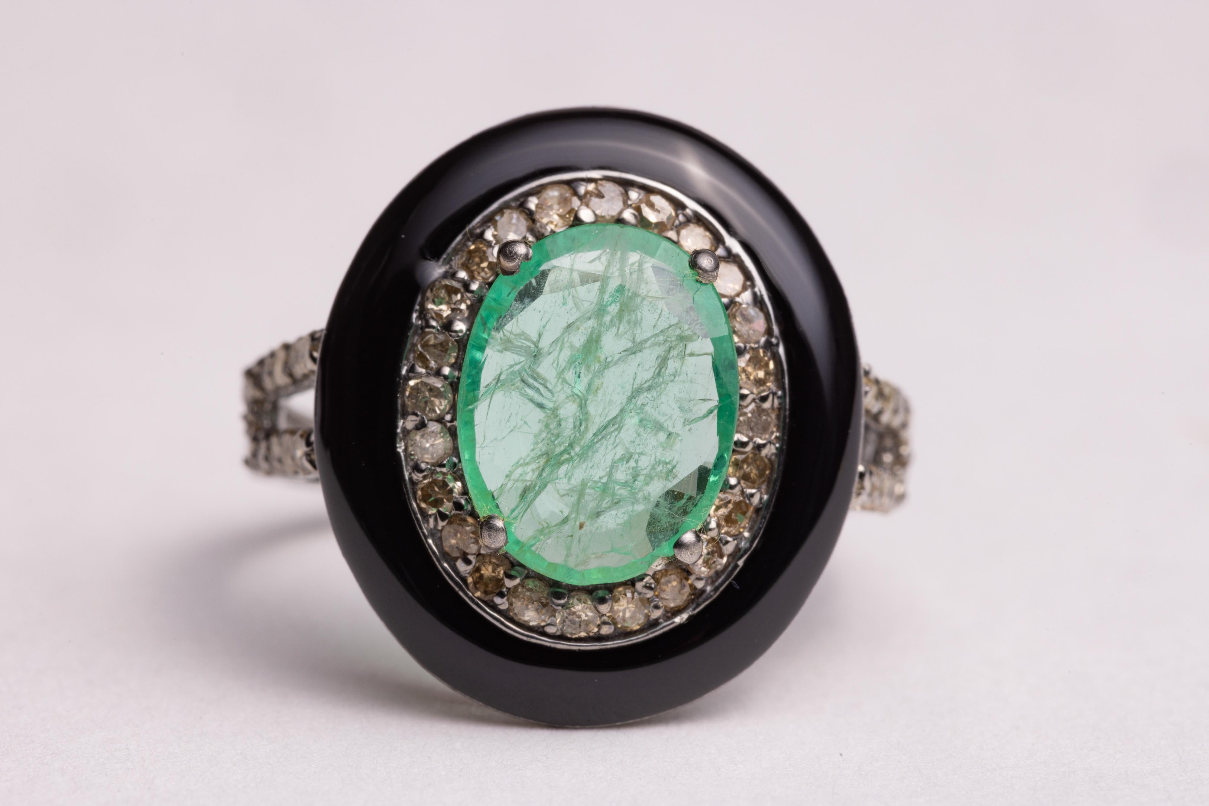 Ein ovaler, facettierter Smaragd, umgeben von runden Diamanten im Brillantschliff und einem Ring aus schwarzem Onyx. Diamanten auch entlang der Schulter des Bandes.  Die Diamanten haben insgesamt 0,60 Karat, die Smaragde 1,7 Karat.  Die Ringgröße