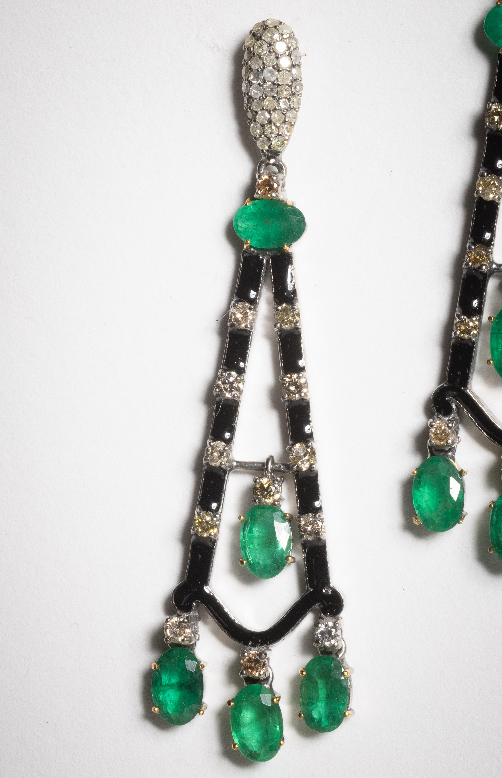 Un delizioso paio di orecchini pendenti con smeraldi colombiani ovali sfaccettati e diamanti rotondi dal taglio brillante, intervallati da smalto nero.  La montatura presenta anche diamanti rotondi sfaccettati con incastonatura a pavé.  In argento