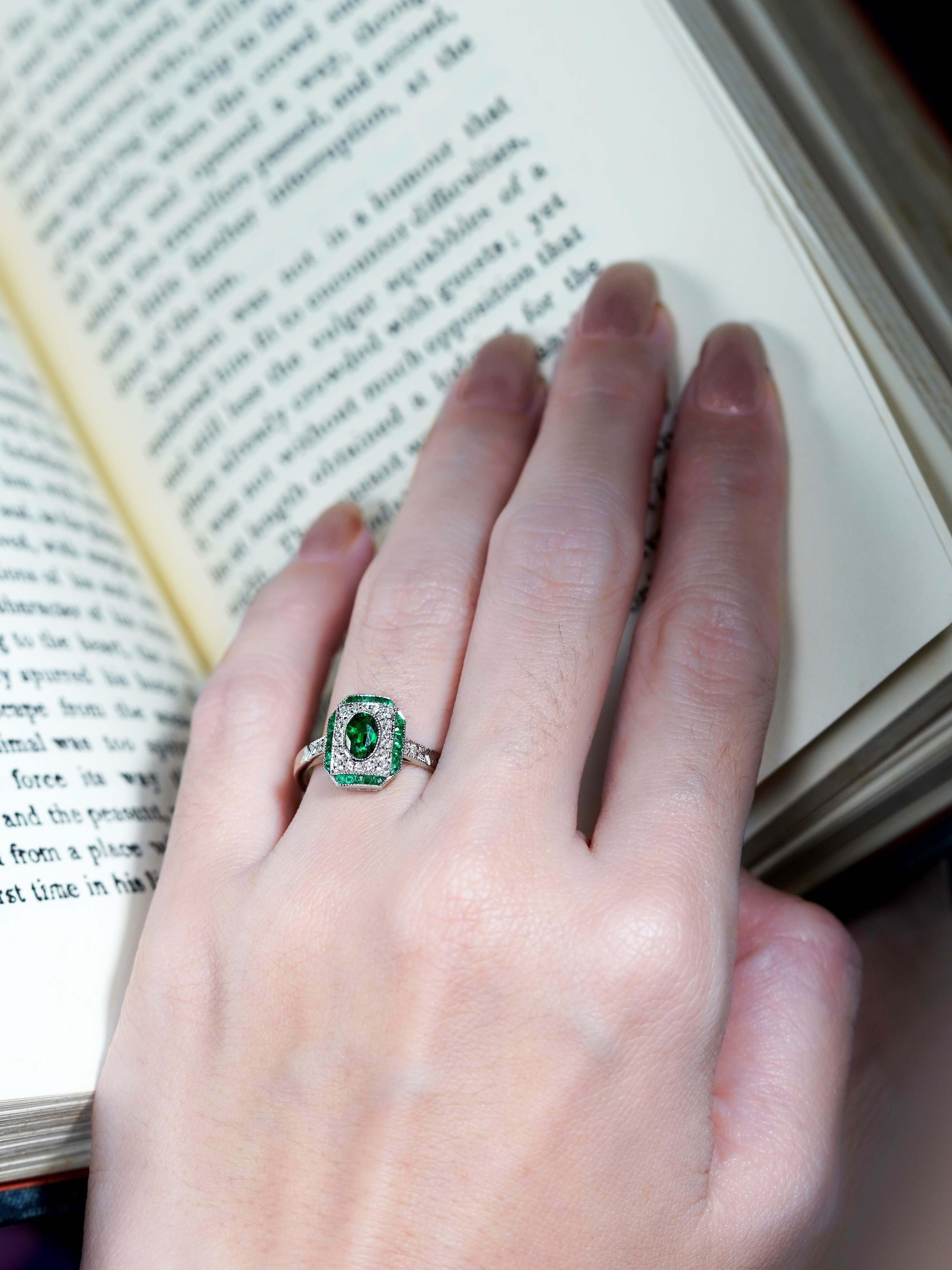 Dieser zeitlose und raffinierte Verlobungsring mit Smaragd und Diamant im Art-Déco-Stil zeichnet sich durch einen ovalen Smaragd von 0,45 Karat aus, der in einer eleganten Lünette gefasst ist. Ein Halo aus funkelnden Diamanten umgibt den