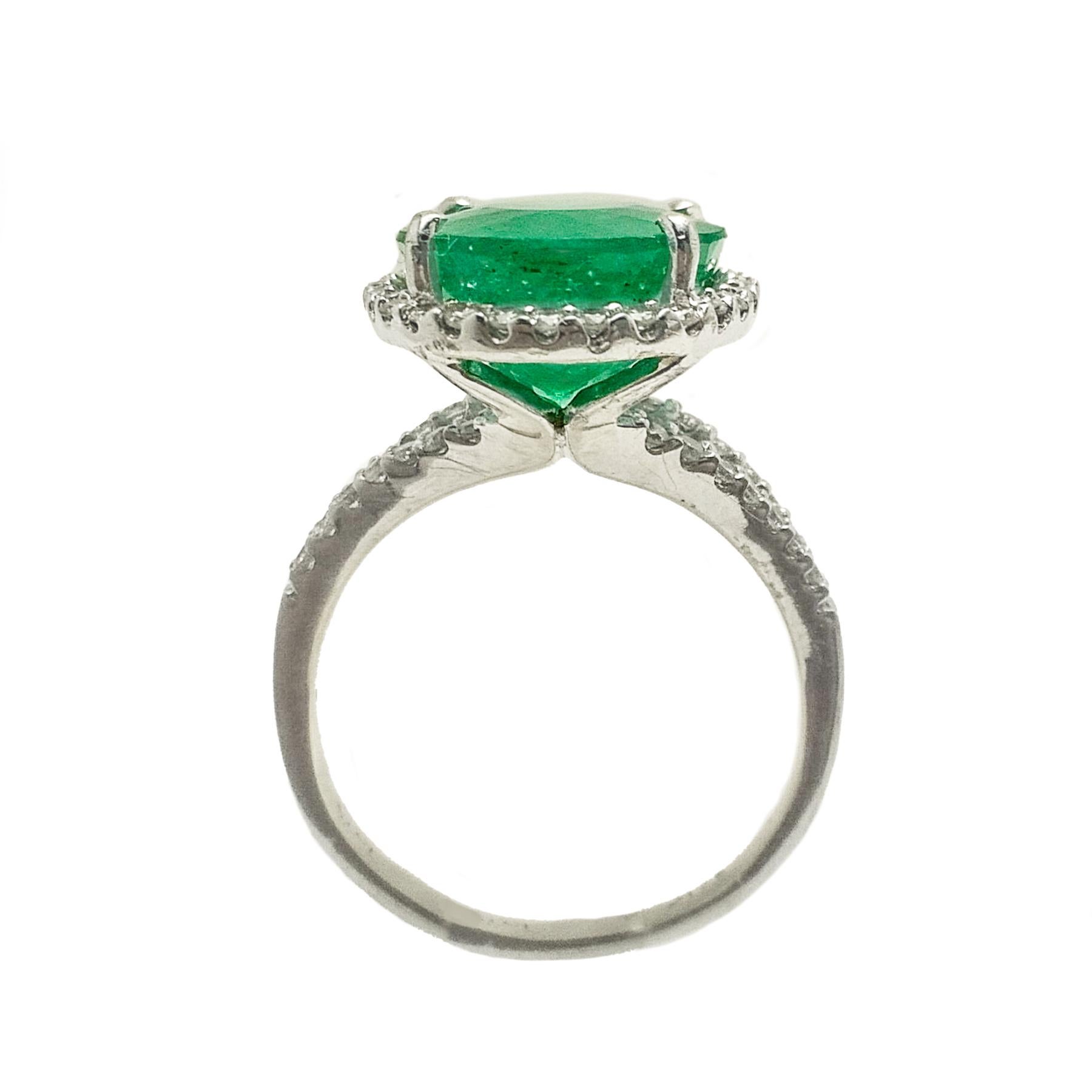 Glamorous emerald diamond ring. Handcrafted green, oval faceted natural emerald encased in open mounting with four round head prongs, accented with round brilliant cut diamond. Beautiful high polished cocktail ring set in 14 karat white gold.