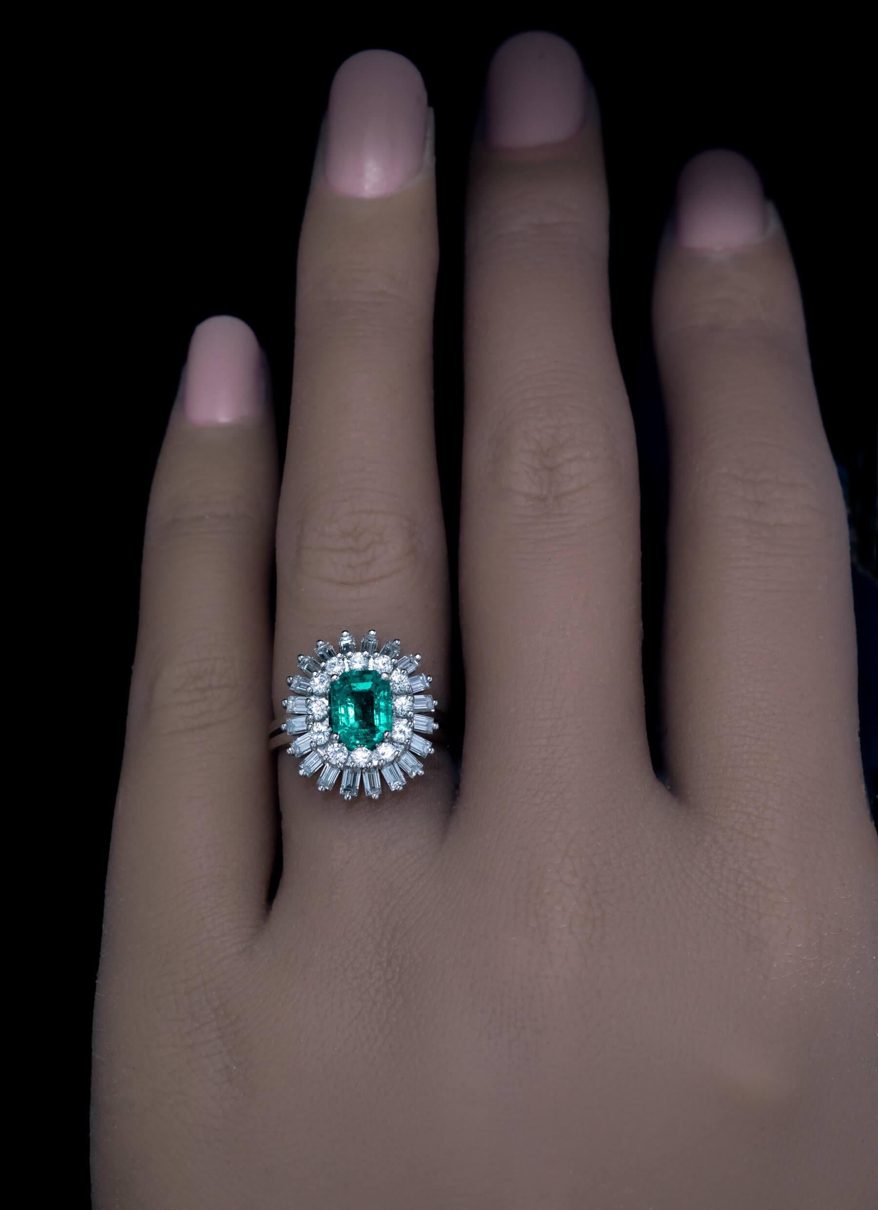 Cette bague de fiançailles en or blanc 18 carats présente une émeraude de 1,35 carat d'une excellente couleur vert bleuté encadrée de diamants ronds de taille brillant (couleur F-G, pureté SI) et de diamants baguettes (couleur E-F, pureté VS) d'un