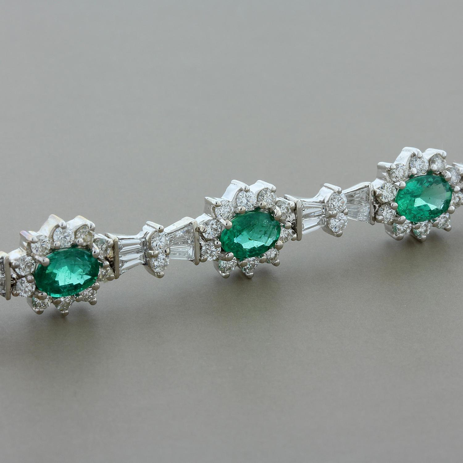 A feminine bracelet featuring 6.47 carats of deep green emeralds. The oval cut emeralds are haloed by 6.15 carats of round cut colorless VS quality diamonds with bows of baguette cut diamonds between each floral cluster. Set in 14K white gold with a