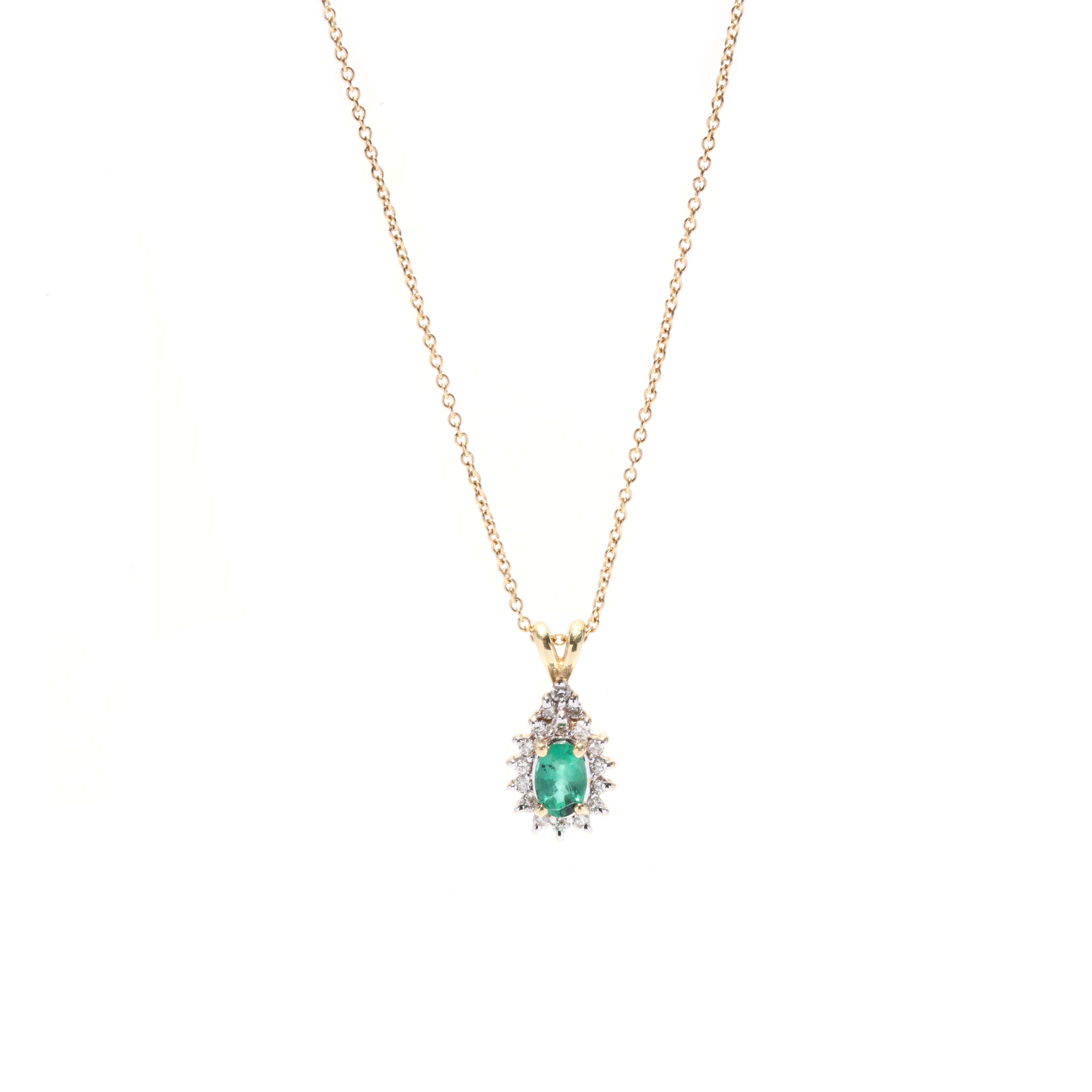 A vintage 14 karat yellow gold emerald and diamond halo pendant necklace. This May birthstone necklace features a prong set, oval cut emerald weighing approximately .50 carat surrounded by a halo of round brilliant cut diamonds weighing