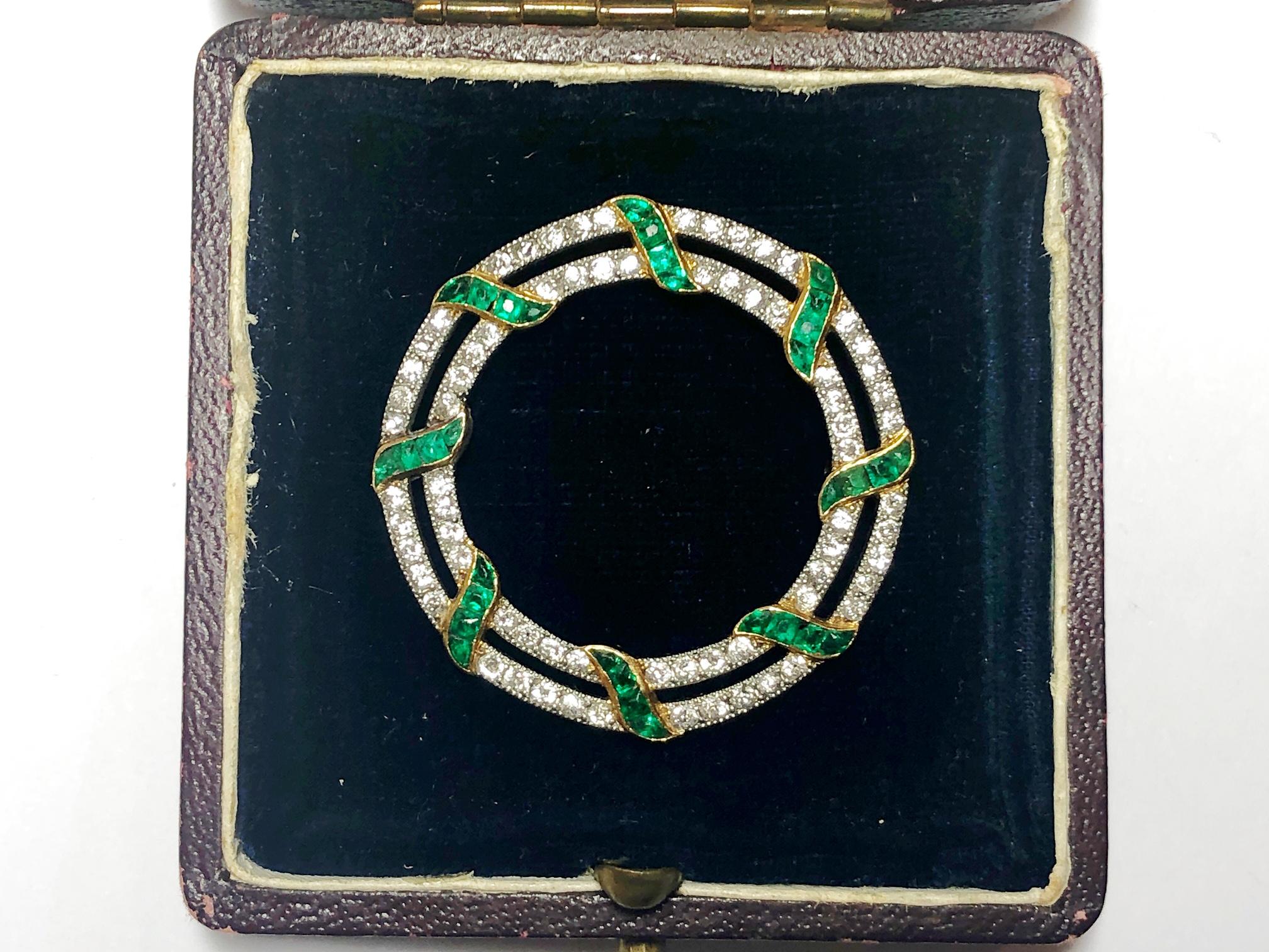 An Edwardian emerald and diamond circular brooch, double openwork circles set with old cit diamonds, mounted in platinum, with calibre cut emerald ribbon detail, in yellow gold, measures approximately 36mm diameter