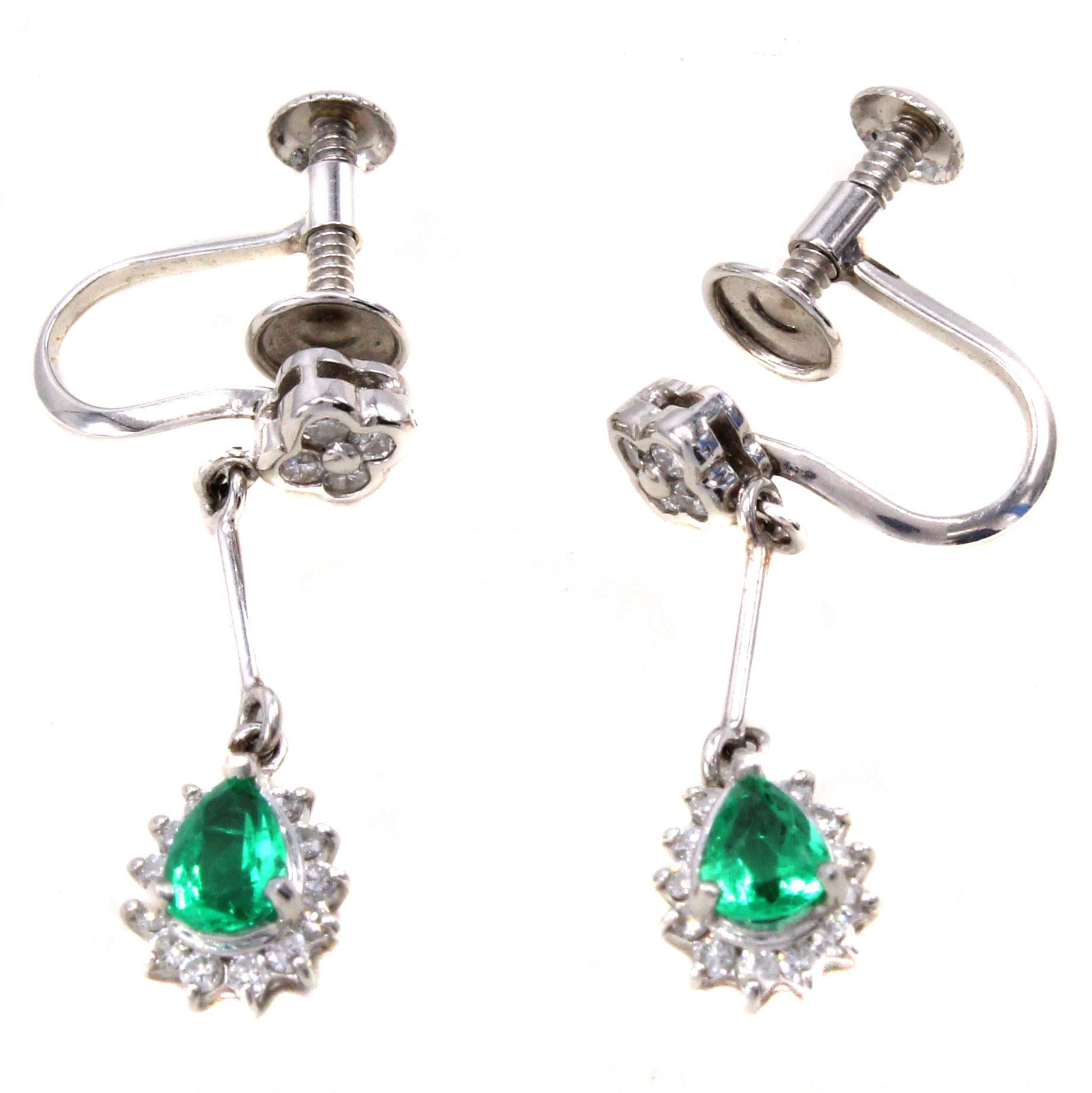 Finely handcrafted in platinum these pendant earrings feature 2 vibrant green lively pear shape emeralds each surrounded by 13 bright white round brilliant cut diamonds. Flexibly connected by a platinum bar to a clover of 4 diamonds, the earring is