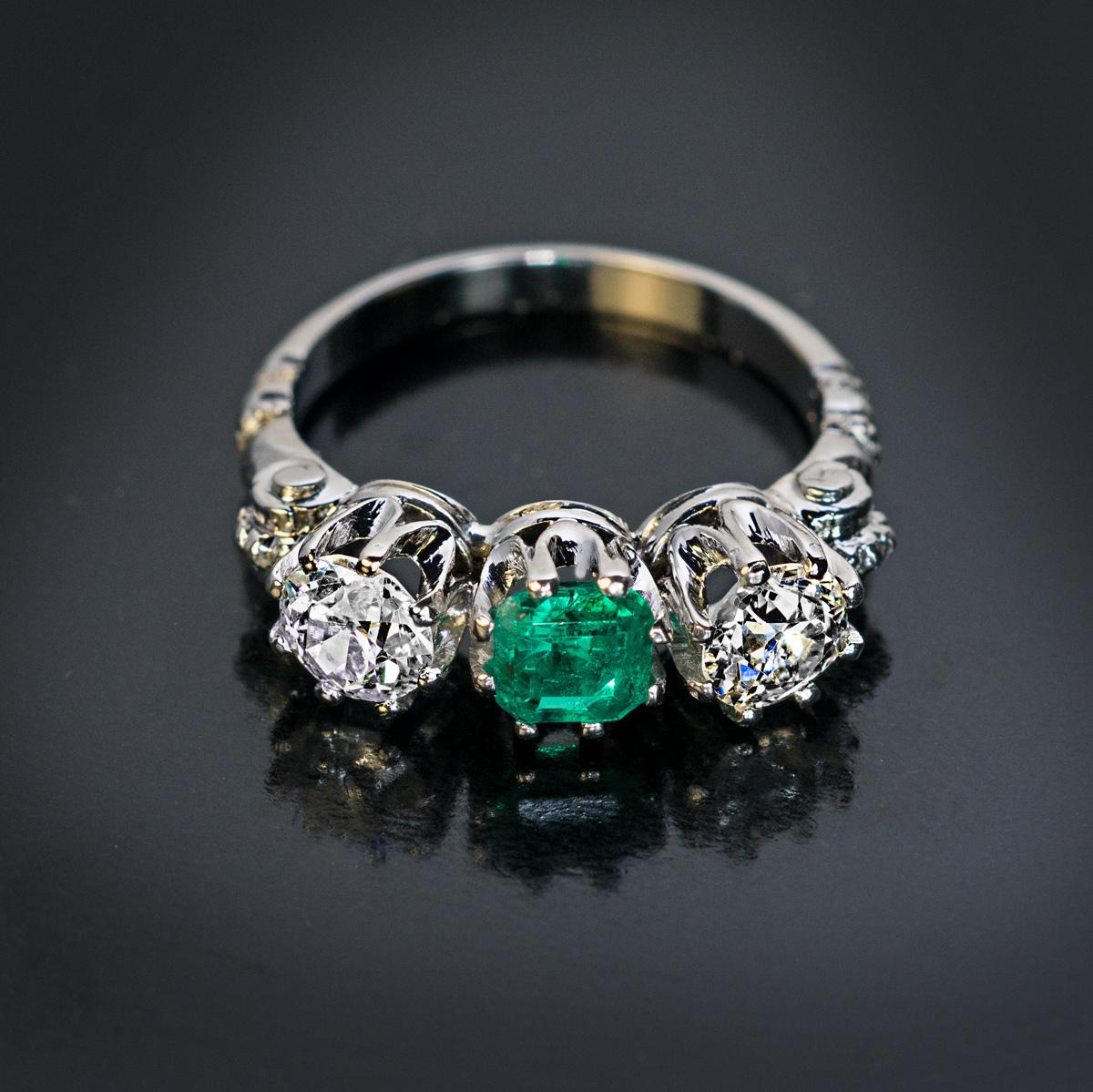 This vintage, circa 1930s, three stone engagement ring is handcrafted in platinum. The ring is centered with a square natural emerald of a vivid bluish green color flanked by two sparkling bright white old European cut diamonds (G-H color, VS2/SI2
