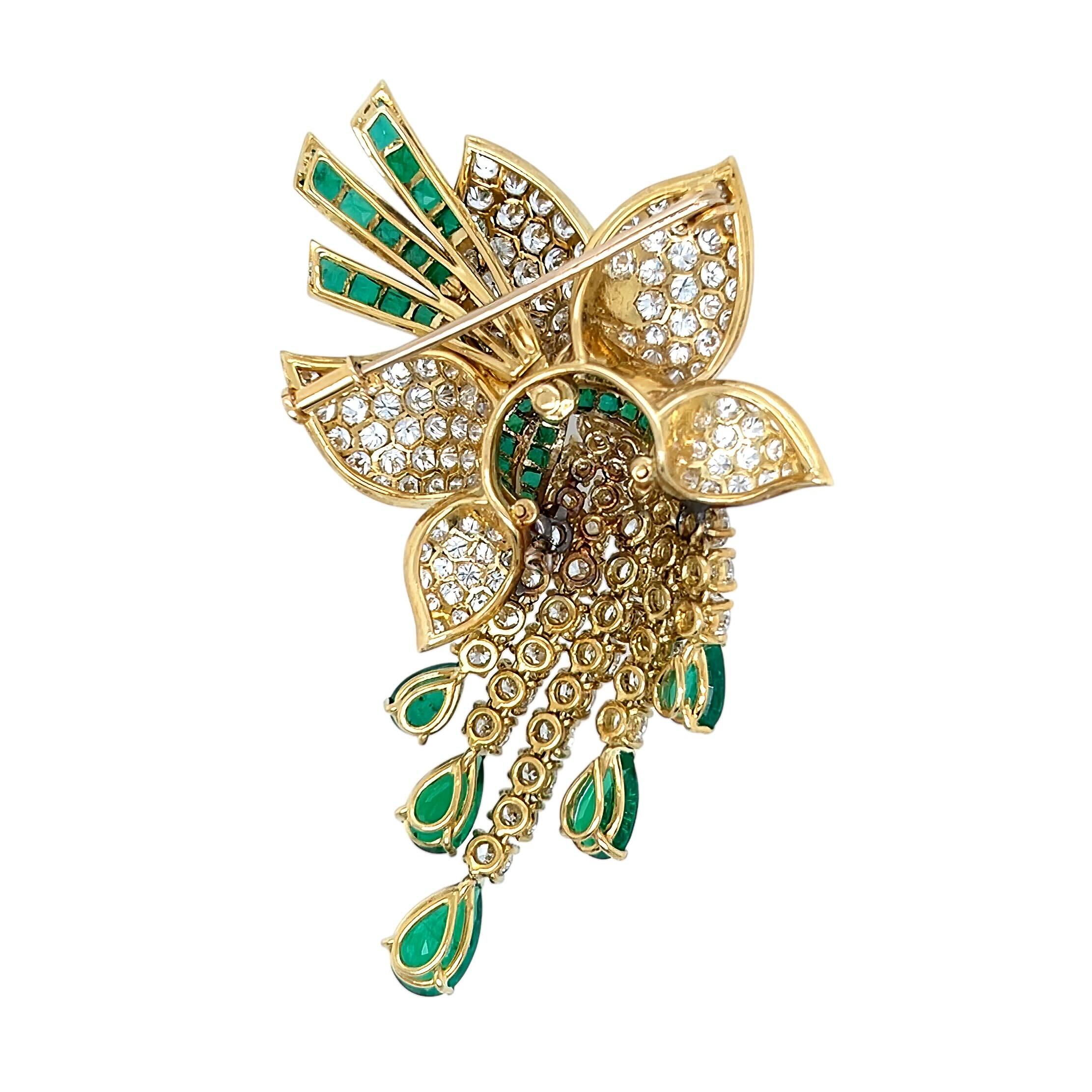 Una spilla in oro giallo 18 carati, smeraldi e diamanti.  Disegnato come un fiore stilizzato con diamanti incastonati che sospende nappe incastonate con diamanti rotondi taglio brillante e che culmina in cinque smeraldi a forma di pera, impreziositi