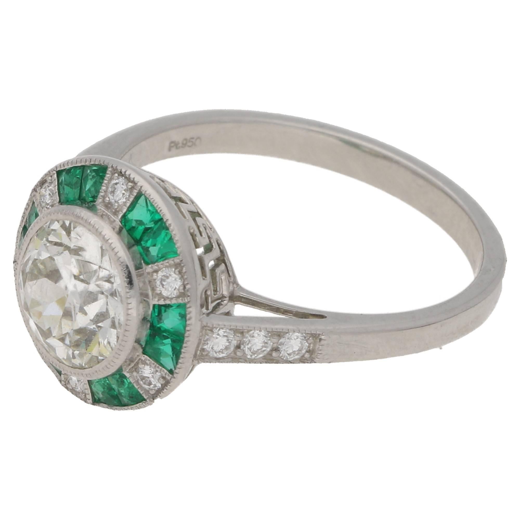 A beautiful emerald and diamond cluster engagement ring in platinum. The ring is formed of an old European cut diamond rubover set to the centre with a millegrain finish. The centre diamond is surrounded by a halo of calibre cut emeralds and round