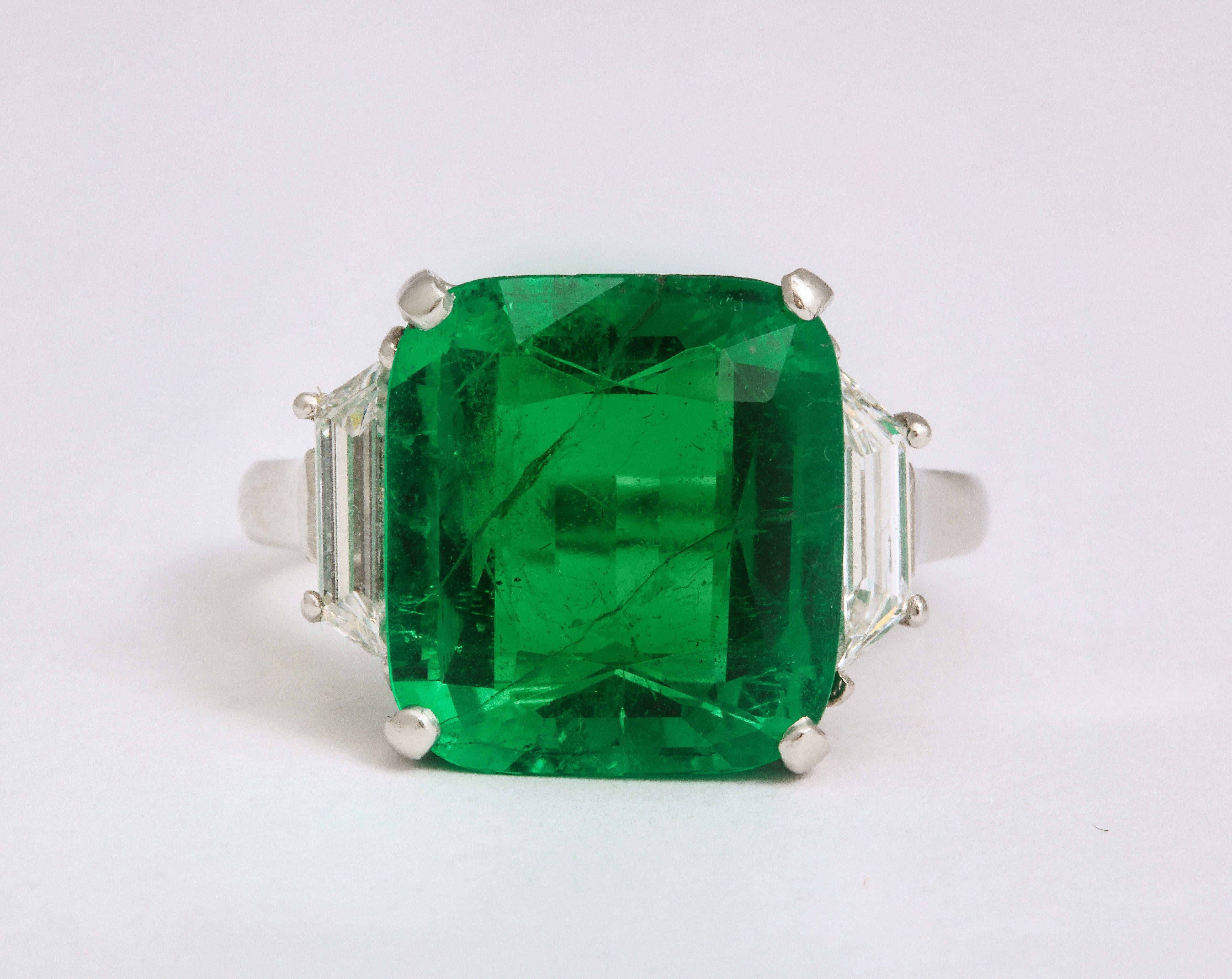 A large and bold 6 cts tw square cut emerald sits between .60 cts tw of trapezoid fine white diamonds in this 18K white gold ring. Currently size 5 1/2, 

Width:
1/2 x 1/2 inch without diamonds
3/4 inch with diamonds 

Height:
3/8 inch 

 