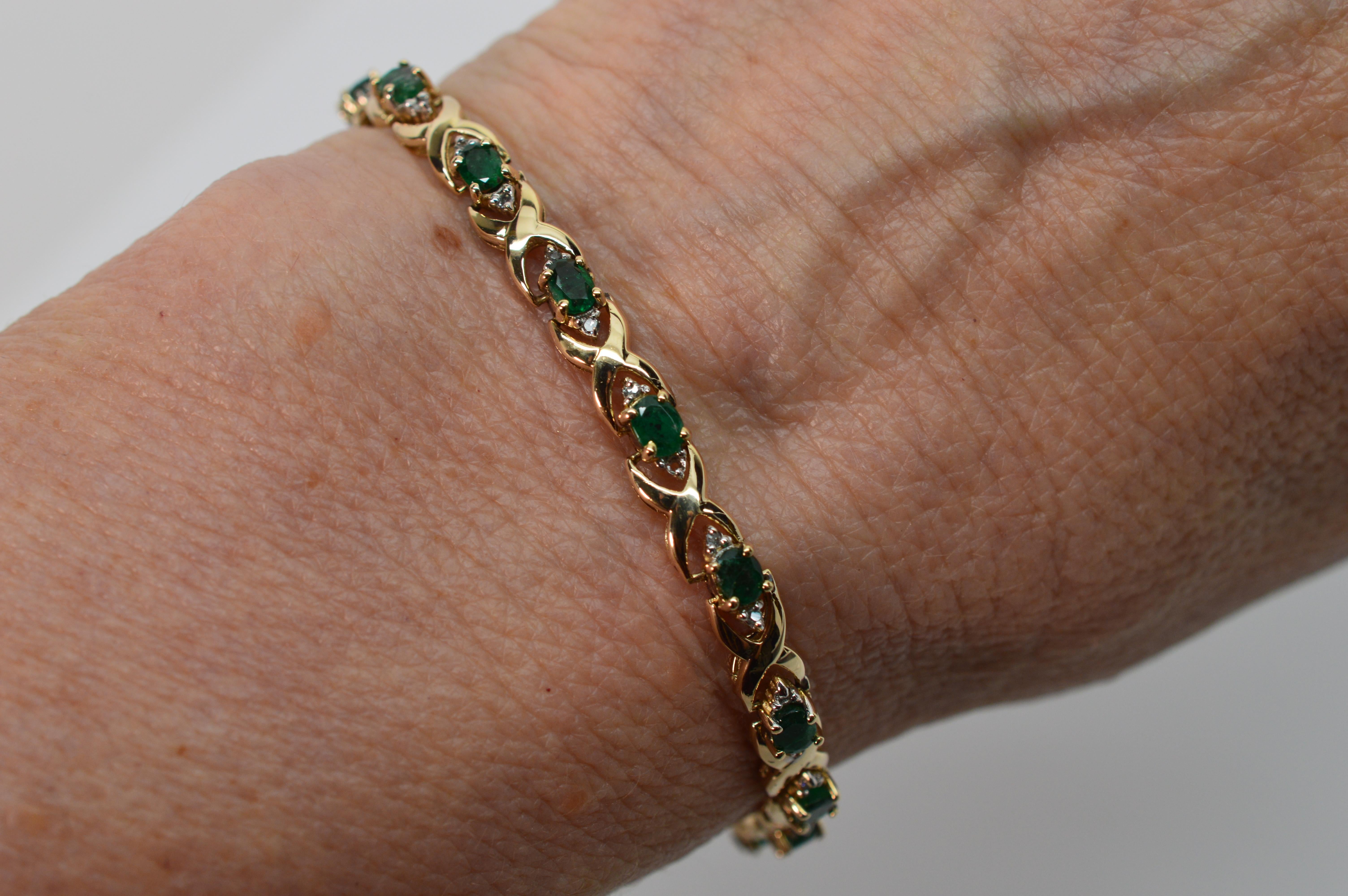Vibrant facet cut oval emerald gemstones are accented with petite diamonds along this seven inch classic tennis bracelet of bright fourteen karat (14K) yellow gold. This slender gold links of this bracelet attractively highlights the depth of color