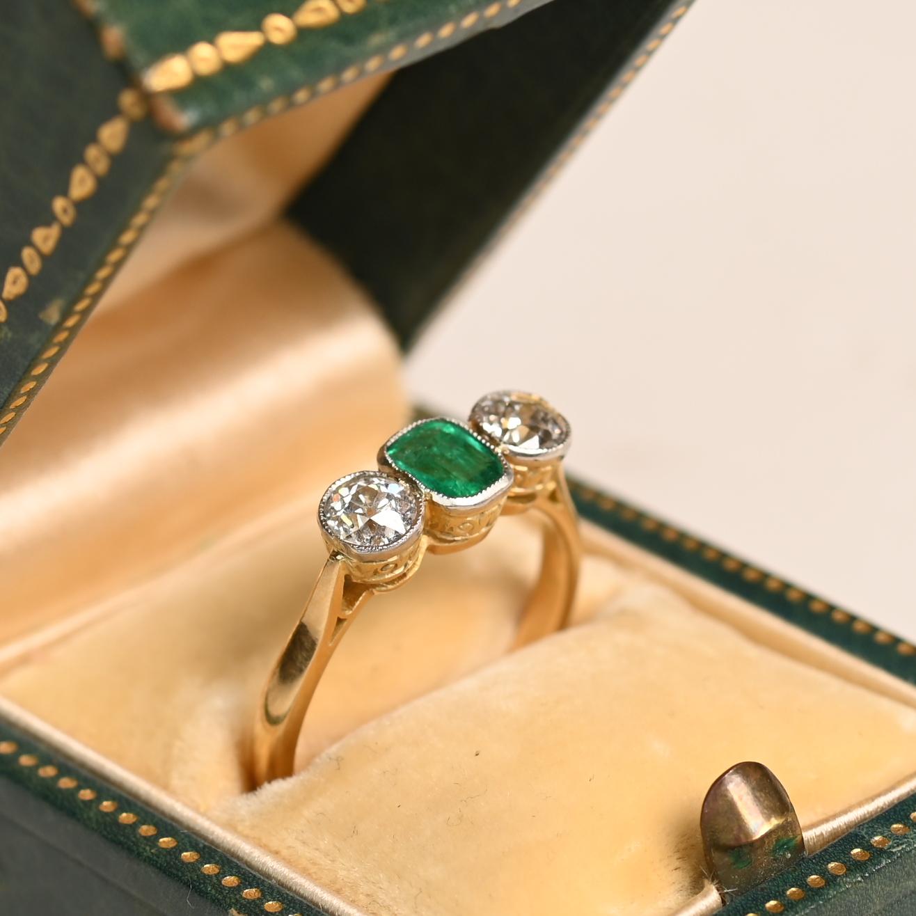 Époustouflante bague �à trois pierres de l'époque édouardienne, vers 1910, ornée en son centre d'une fascinante émeraude naturelle taillée en coussin. La pierre précieuse d'un vert éclatant, pesant environ 0,7 carat, est solidement sertie, ce qui