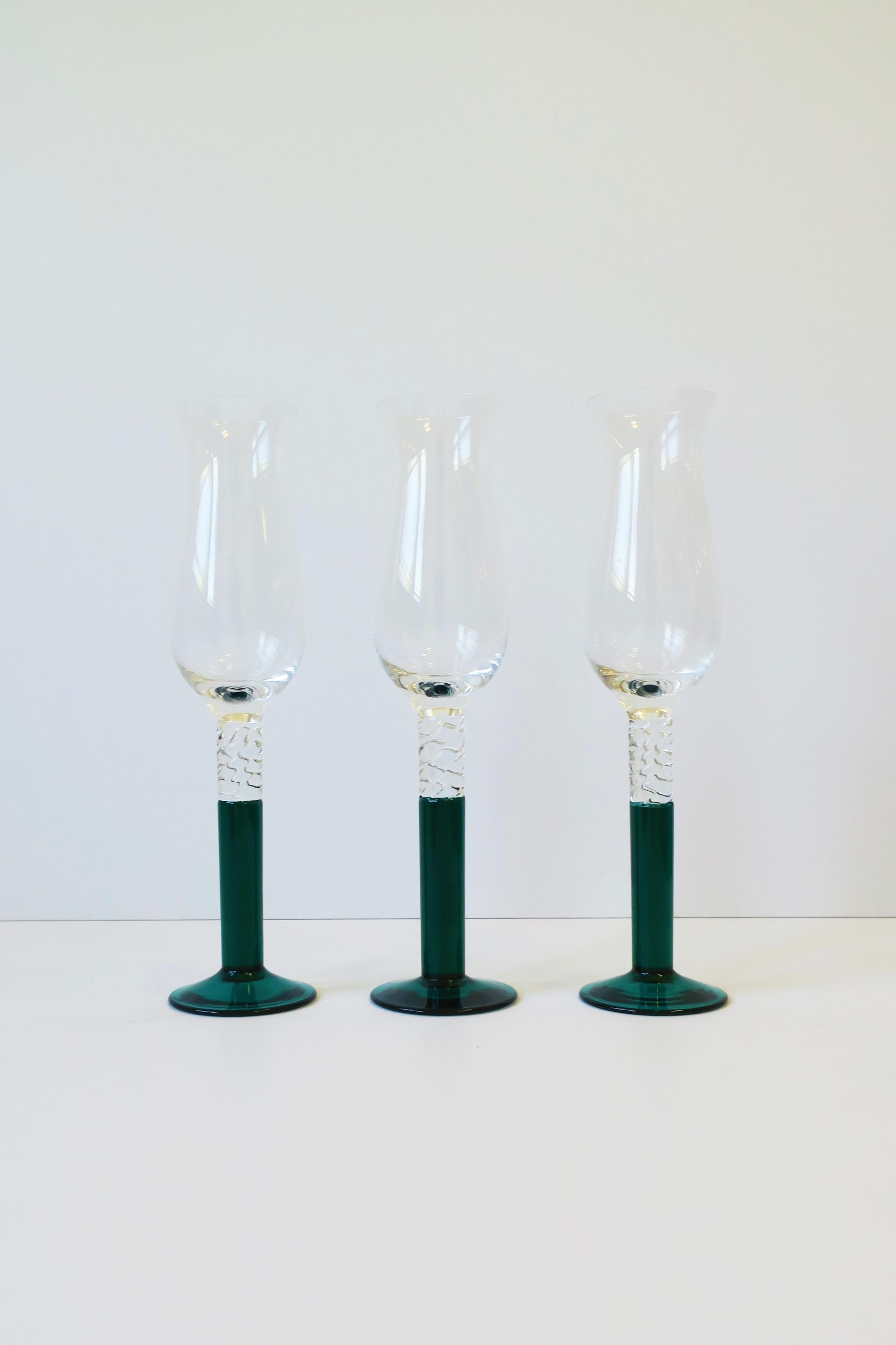 A beautiful set of three (3) Emerald-teal green art glass Champagne flutes glasses, circa 1990s, Europe. In the style of Kosta Boda, Sweden. Colors include: teal green and clear/transparent art glass. A beautiful set for home, summer, holiday