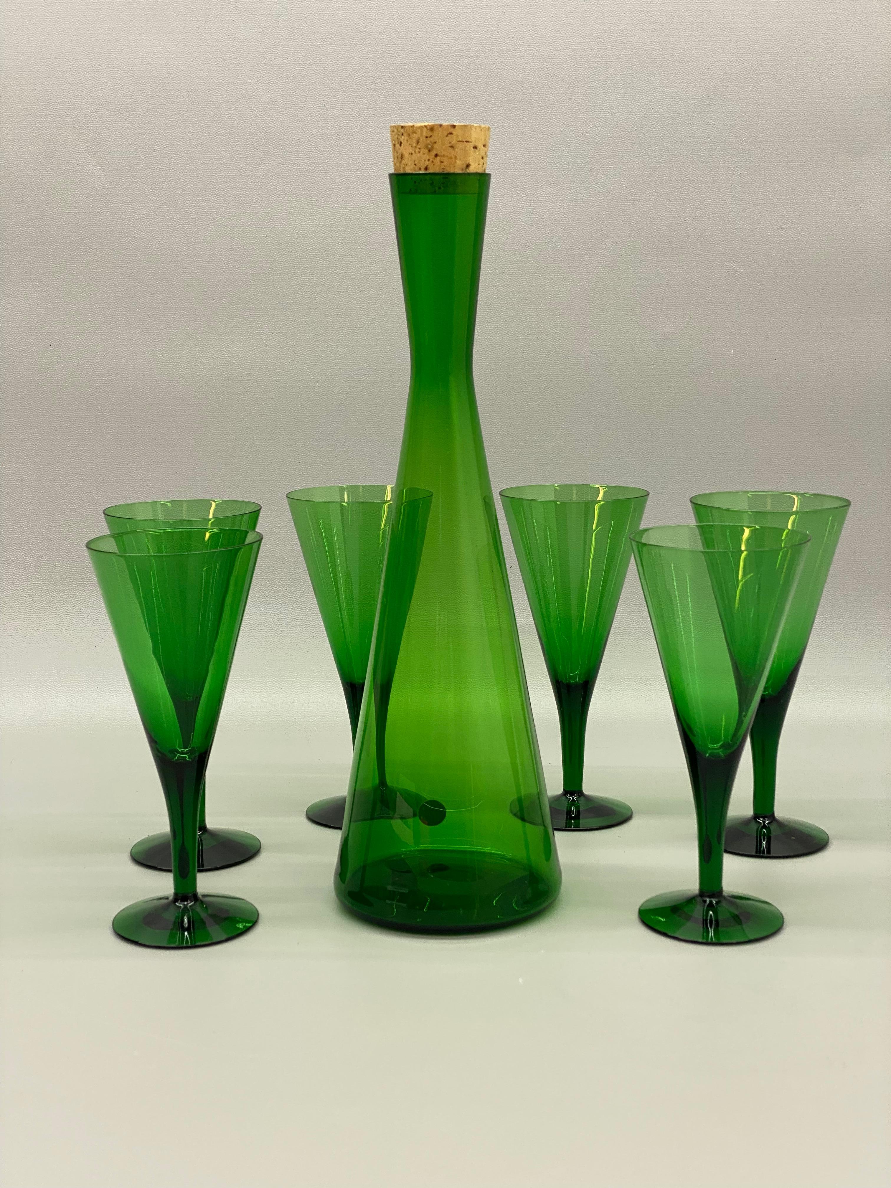 Fino y prístino juego de seis copas acanaladas verde esmeralda y decantador alto. El decantador está firmado con la etiqueta de papel original, By Appointment to H. H. The King of Denmark, Made in Denmark, Kastrup, Holmegaard, 62. Una verdadera