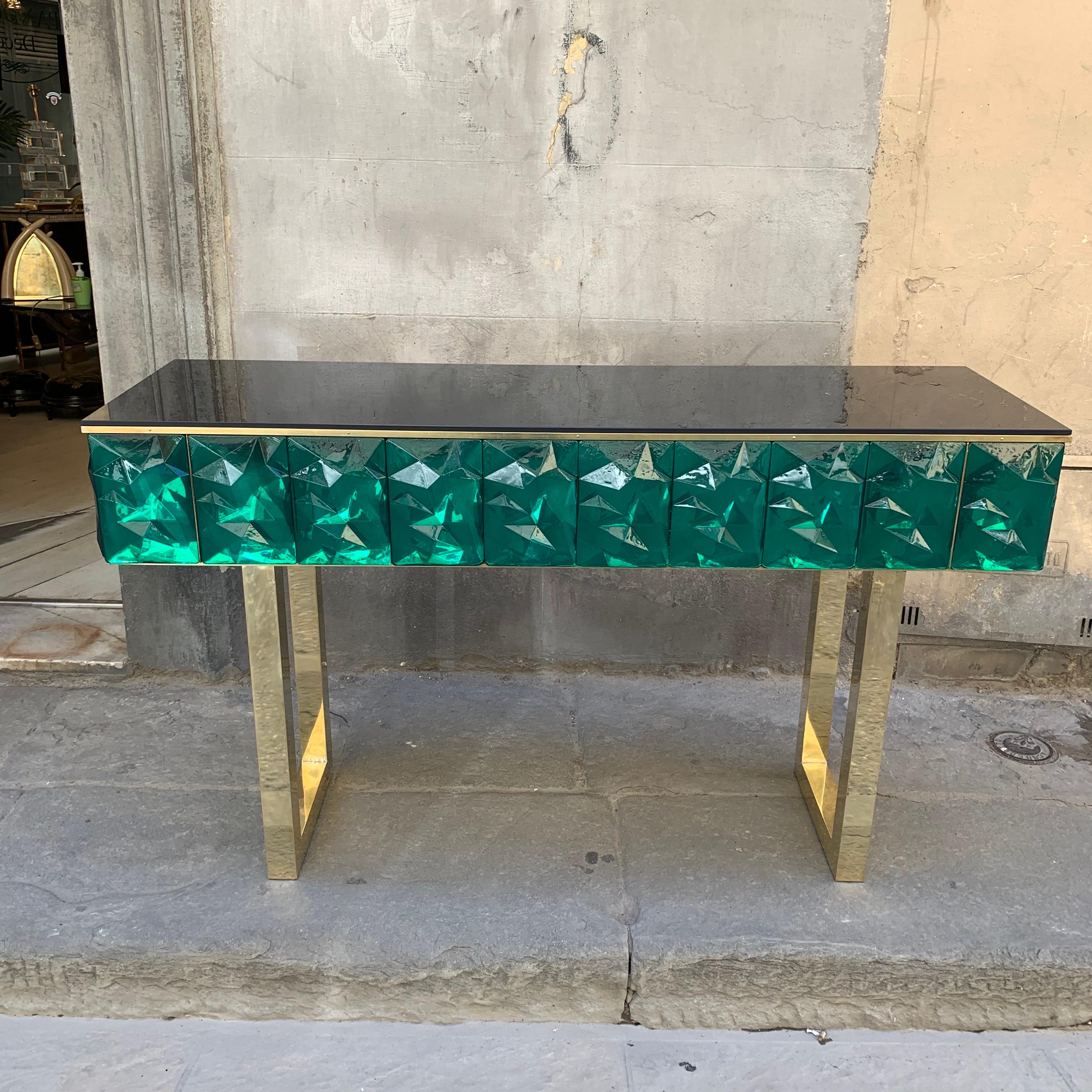 Consola contemporánea de cristal esmeralda con tapa de cristal opalino negro y patas de latón.
El cristal de Murano verde esmeralda tiene una forma facetada efecto diamante, la luz que lo atraviesa crea un sorprendente efecto centelleante.
Diseño