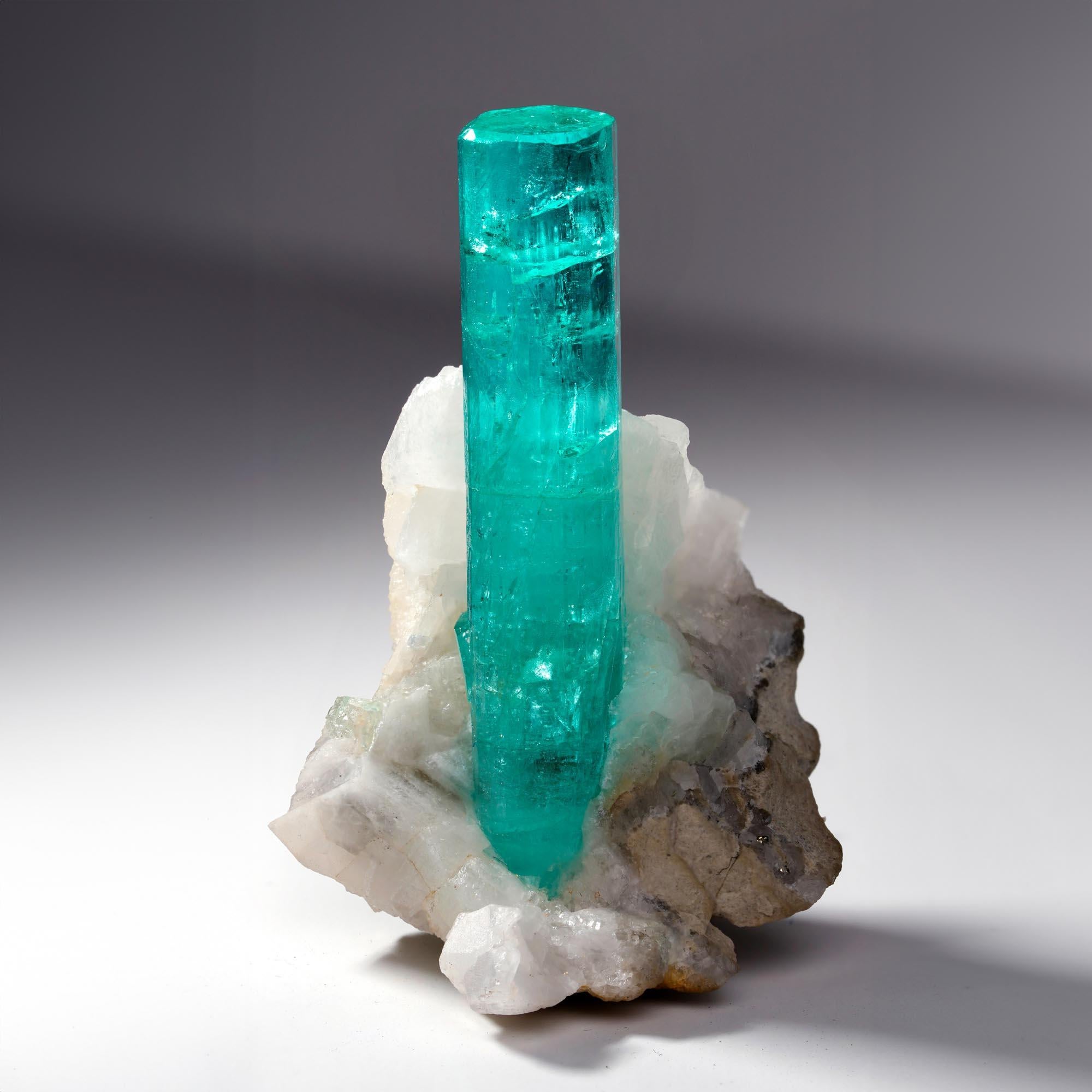 This superb Emerald on Calcite specimen from Colombia showcases a striking, elongated crystal with vibrant green color and excellent transparency. Rising prominently from its contrasting white Calcite matrix, the crystal is sharply terminated and