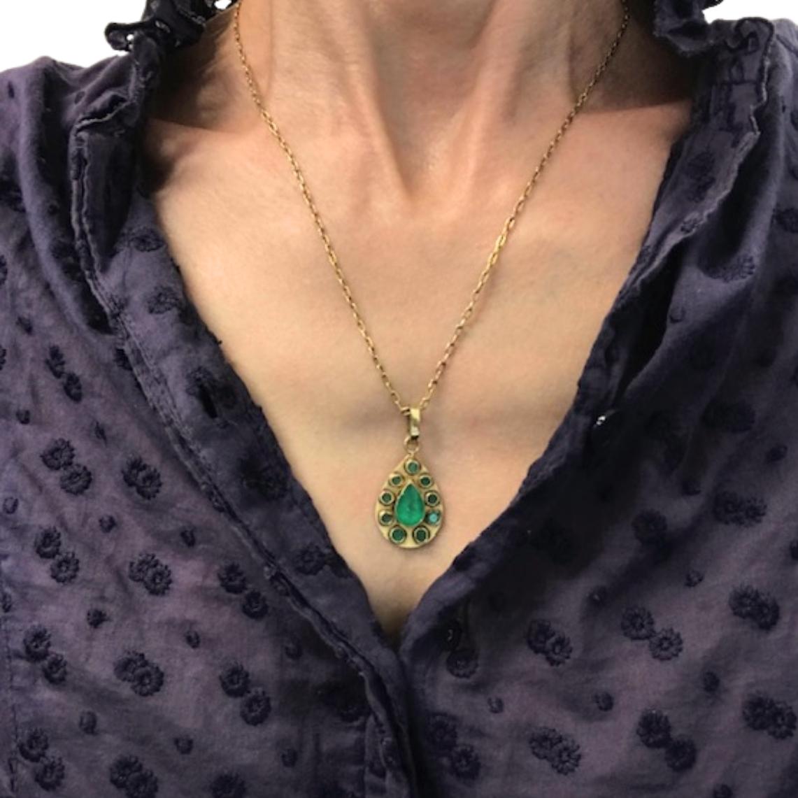 Ce collier vintage présente un pendentif en forme de goutte d'eau serti en or jaune 14k et orné d'émeraudes naturelles. Au centre se trouve une émeraude en forme de poire encadrée par une bordure de huit émeraudes rondes. La monture en or a un ton