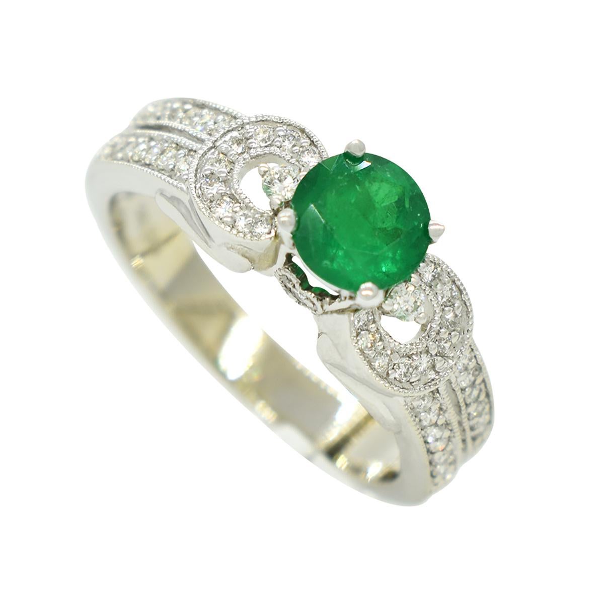 This emerald and diamond ring is a masterpiece crafted from solid 14K white gold. Its focal point is a stunning 0.67-carat round-cut emerald, radiating a deep, mesmerizing dark green hue. The emerald's intense color saturation commands the